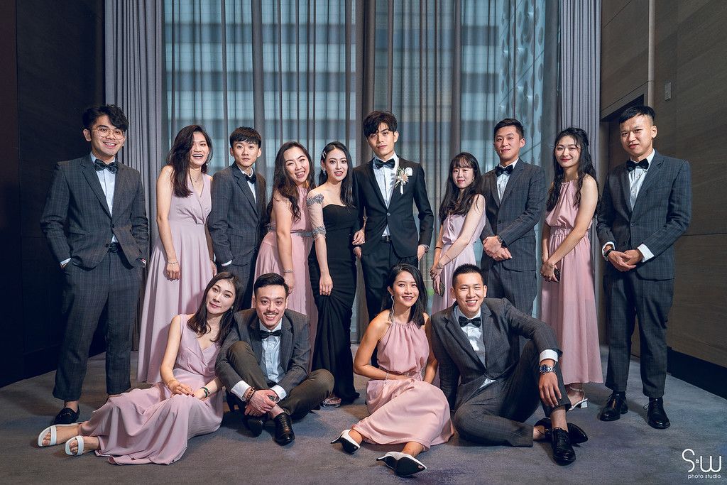 Wedding party in formal attire posing together indoors with bridesmaids in pink dresses.