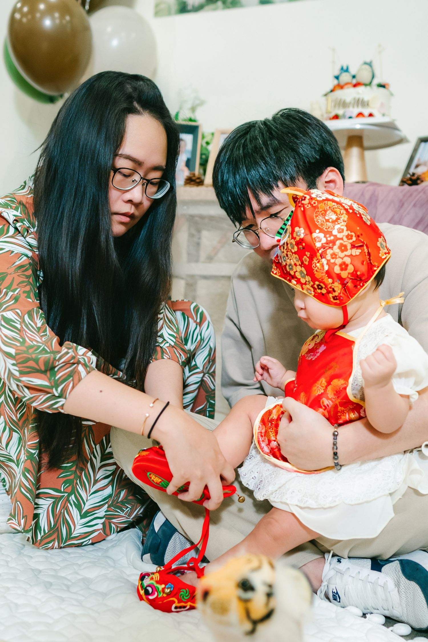 Two people in traditional Asian attire sit together playing with a red decorative object.