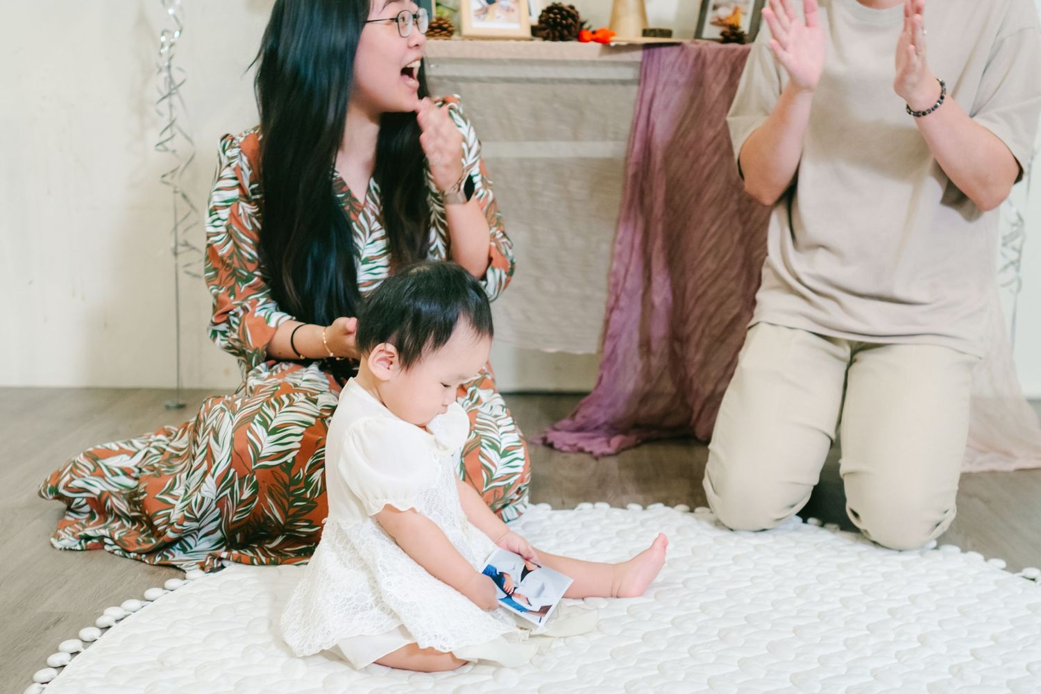 People sitting on a white rug play and laugh together during an indoor family moment.