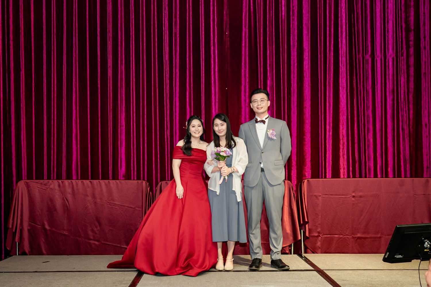 Students perform onstage during a school theater production with red curtains in the background.