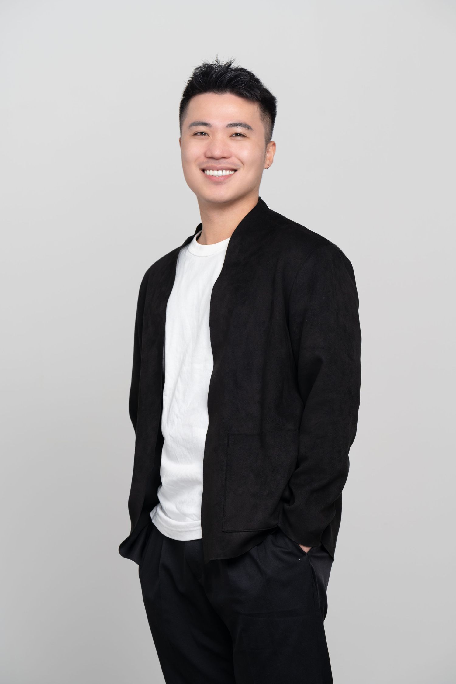 Professional studio portrait of someone wearing a black blazer and white t-shirt against a light gray background.