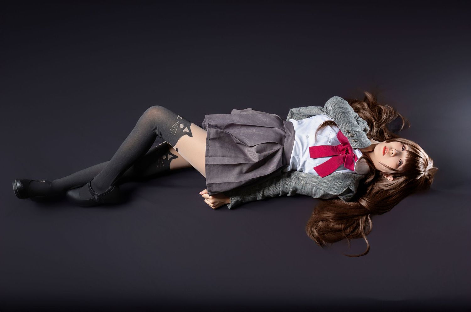 Figure lies on dark floor wearing school uniform style outfit with gray skirt and long socks in dramatic lighting.