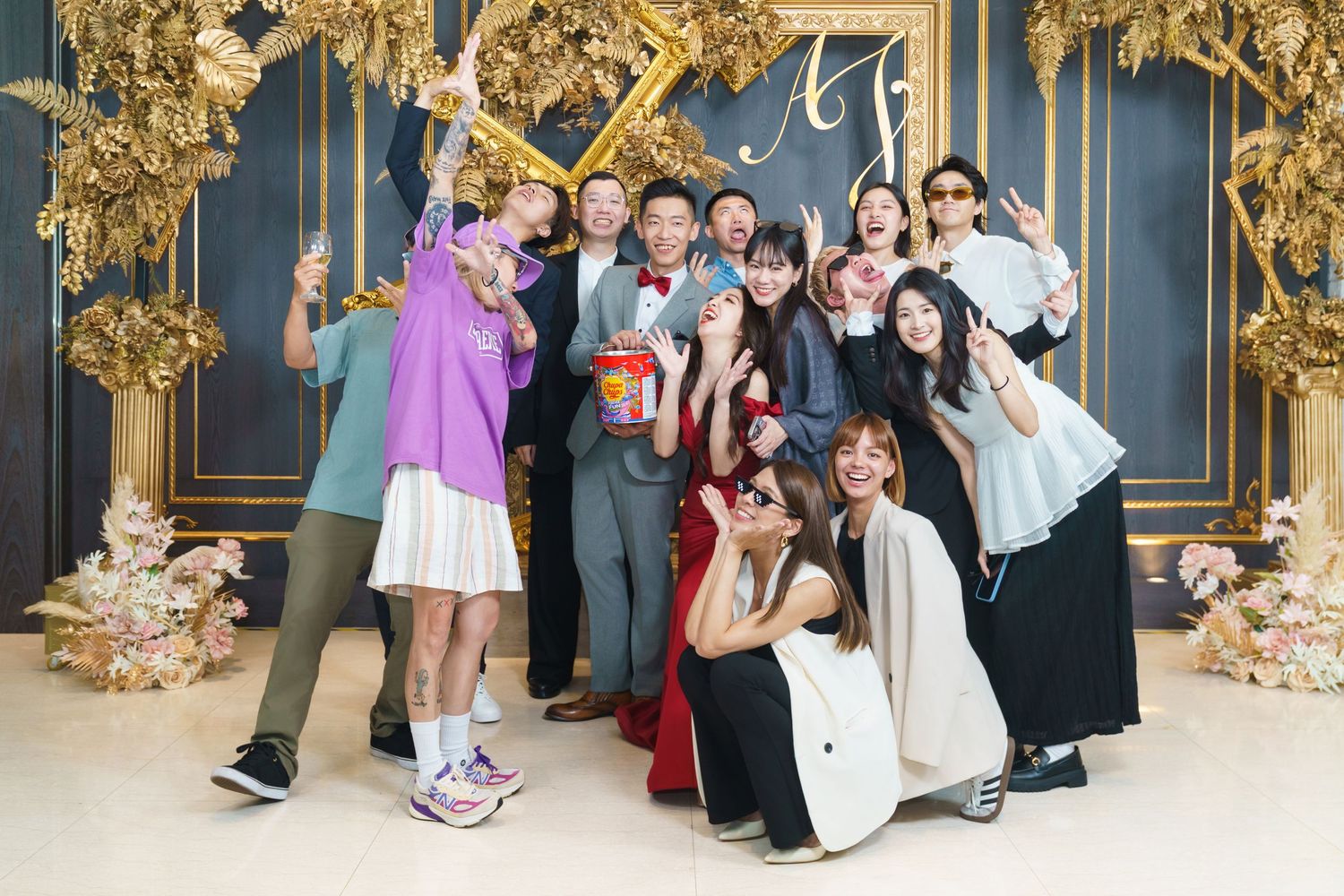 A fun group photo of people posing playfully in formal attire against an ornate gold and blue wall backdrop.
