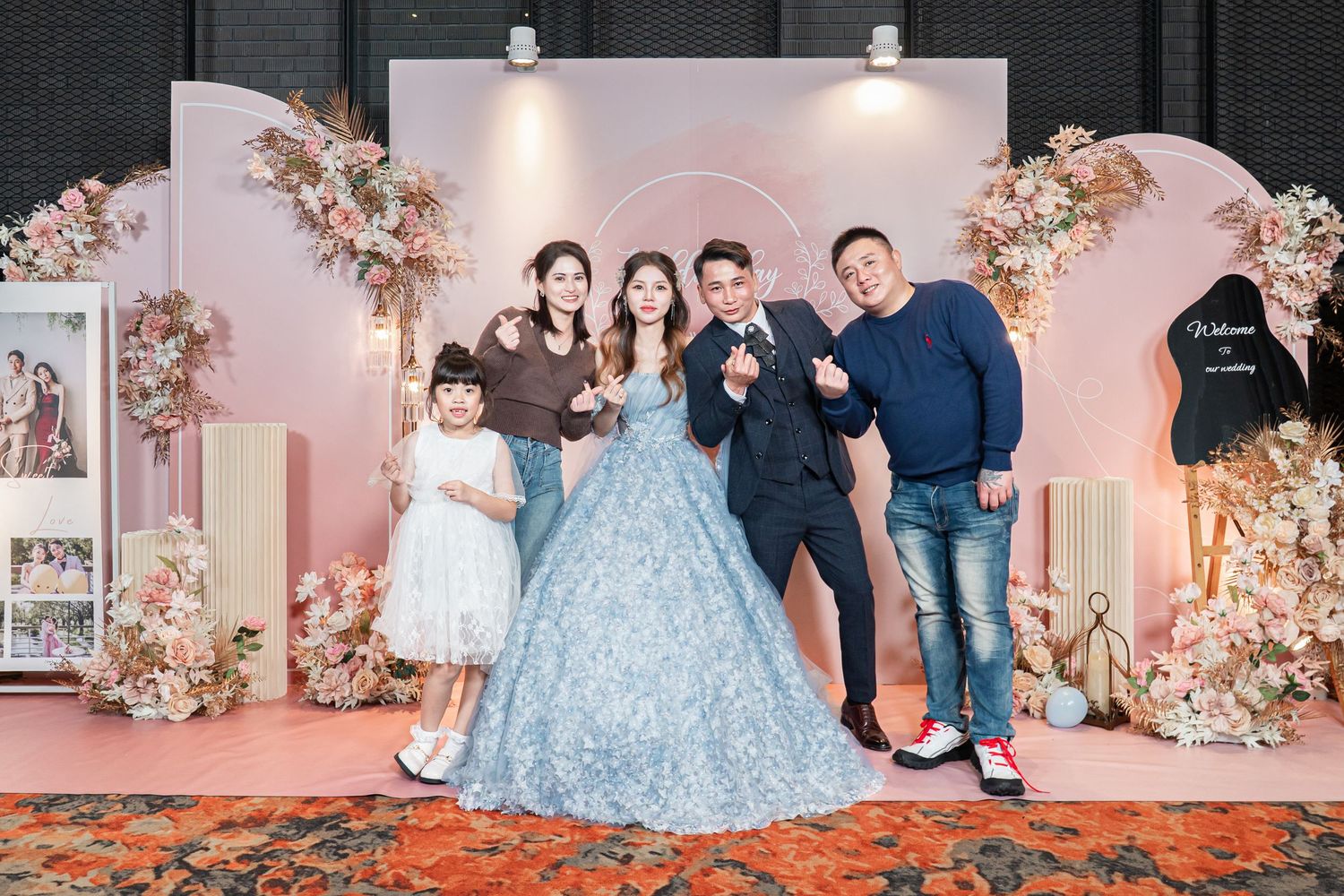 Group poses at elegant pink floral decorated event backdrop with ballgown and formal attire.
