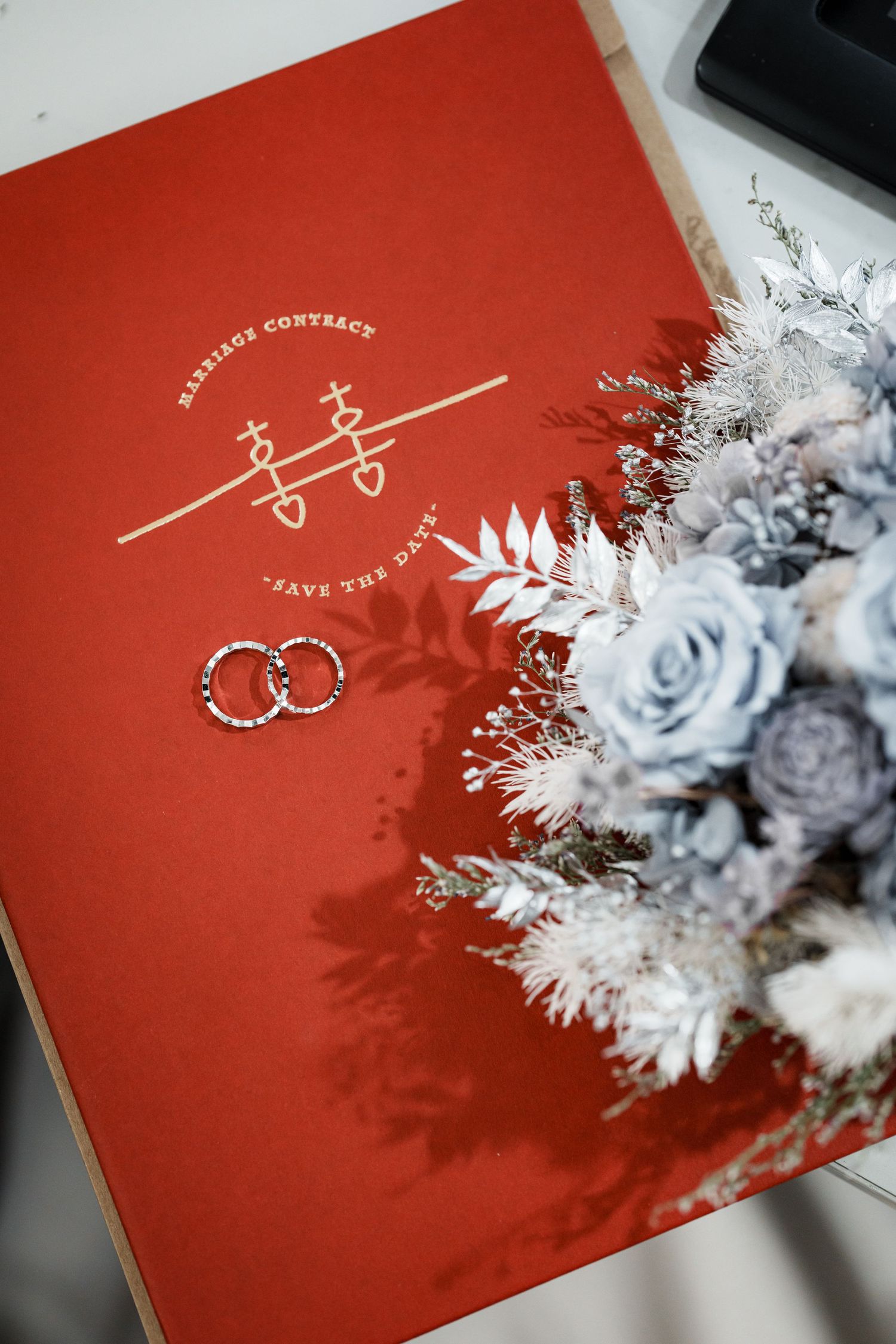 A red wedding invitation album decorated with delicate white and blue dried flowers on the cover.