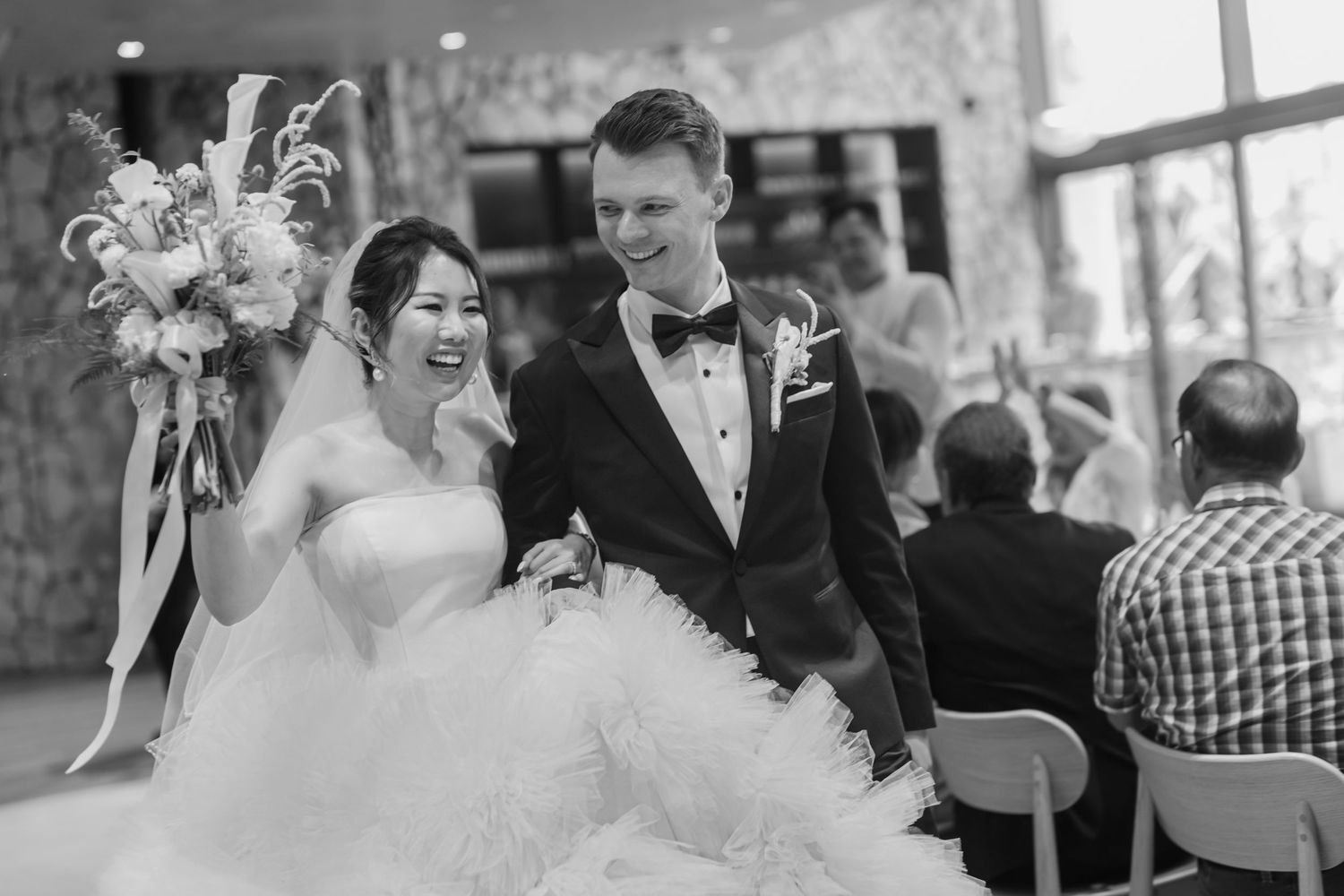 A joyous wedding celebration with guests and newlyweds sharing laughter at an intimate indoor venue.
