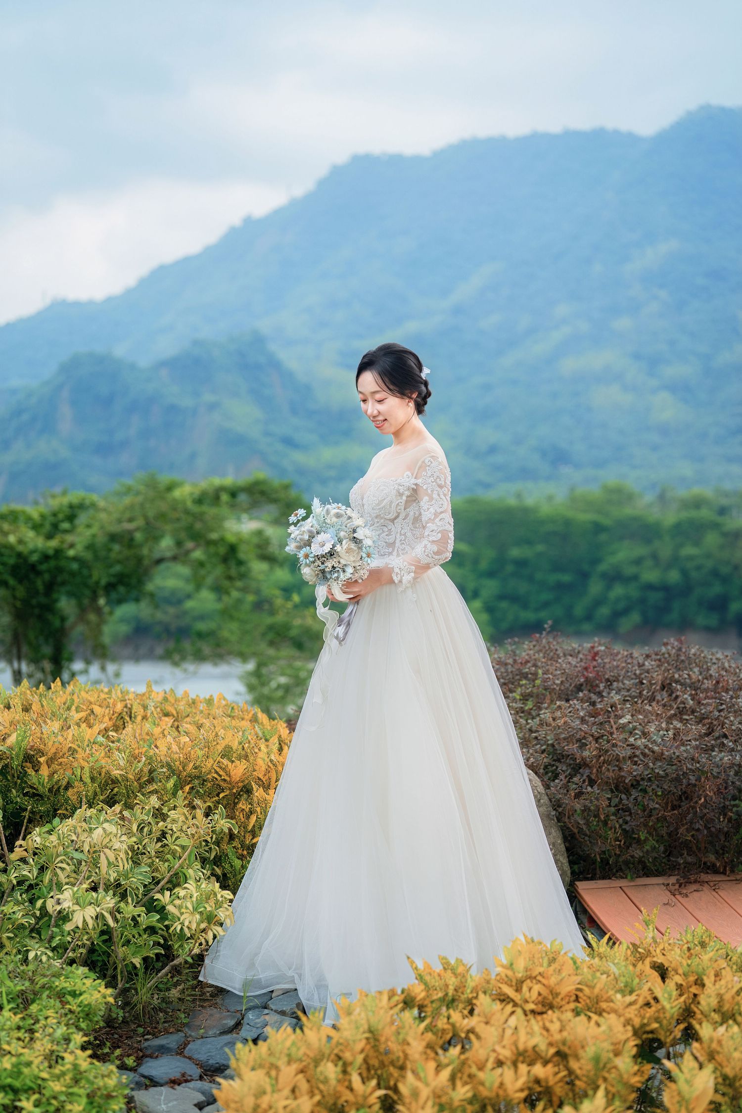 Elegant white wedding gown photographed against scenic mountain landscape with vibrant yellow flowers in foreground.
