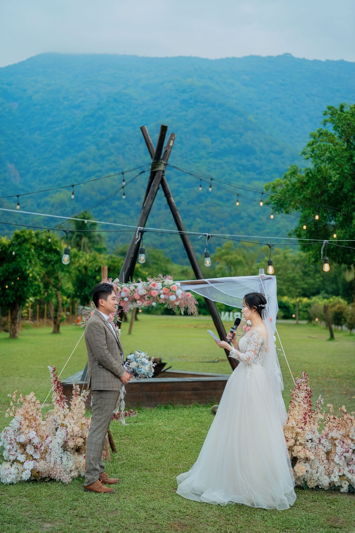 A romantic outdoor wedding scene with a couple dancing in a grassy field with mountains in the background.