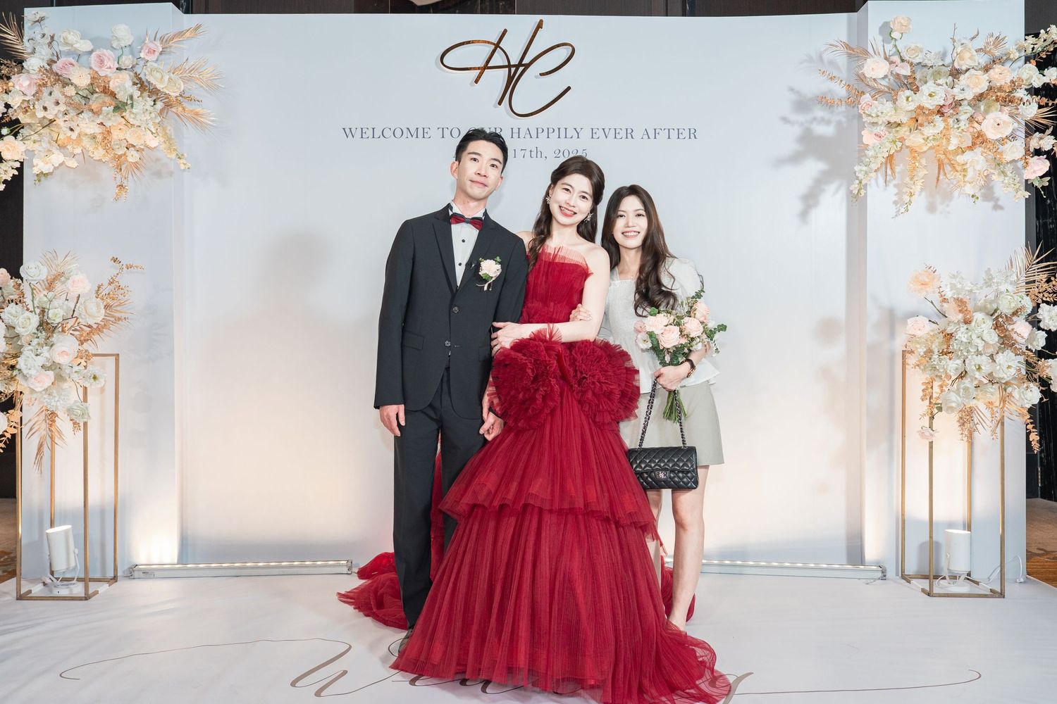 Elegant couple poses for formal portraits in a white studio with cherry blossoms and a burgundy red ballgown.