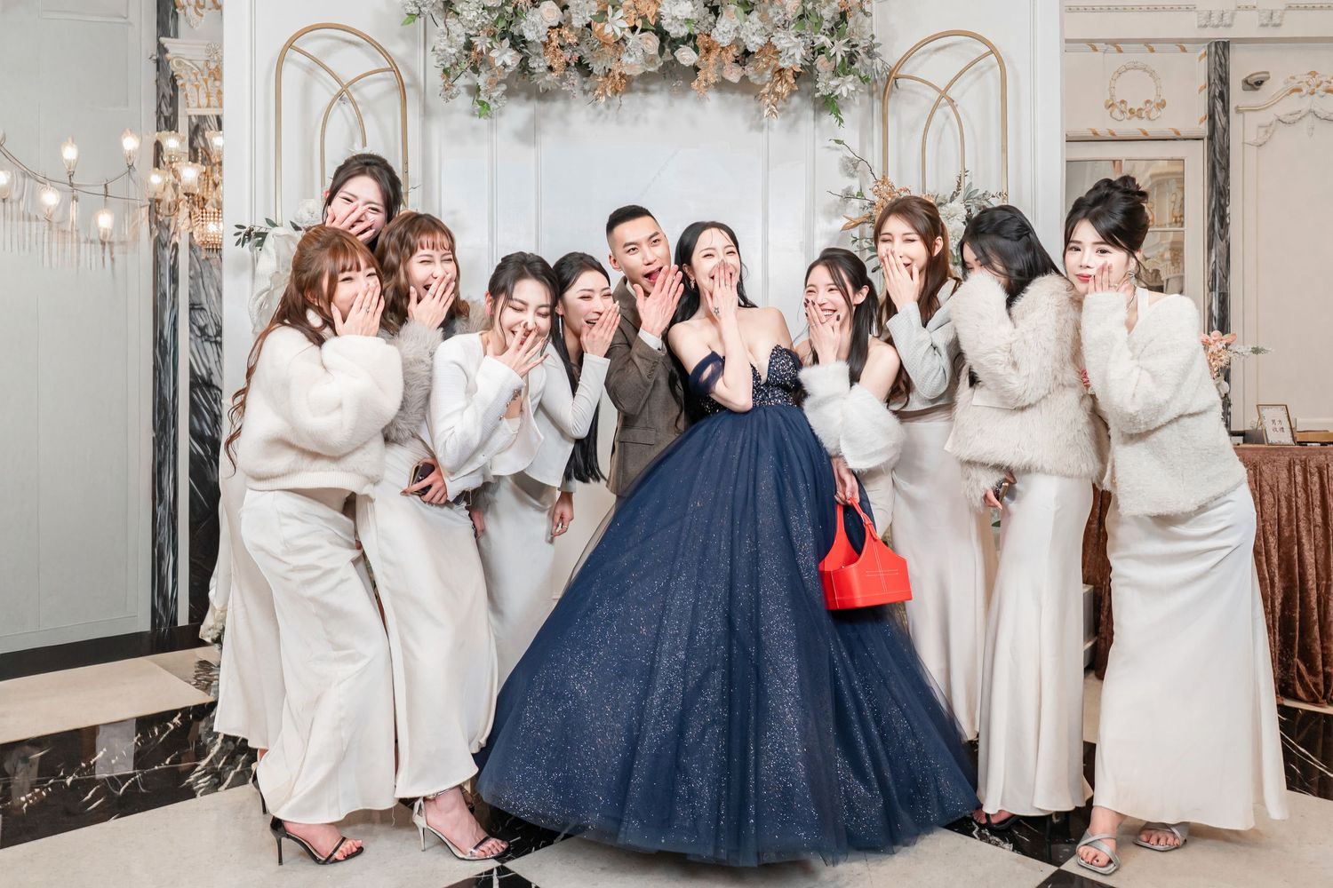 A group in white robes and navy blue dresses pose together in a formal setting with elegant decor.