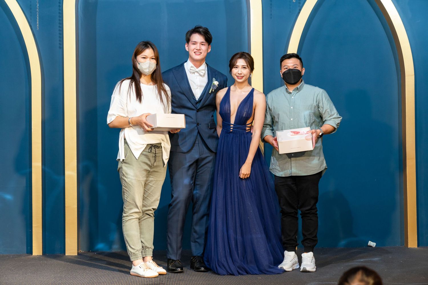 Four people stand together against a blue backdrop with gold arch details at a formal event.