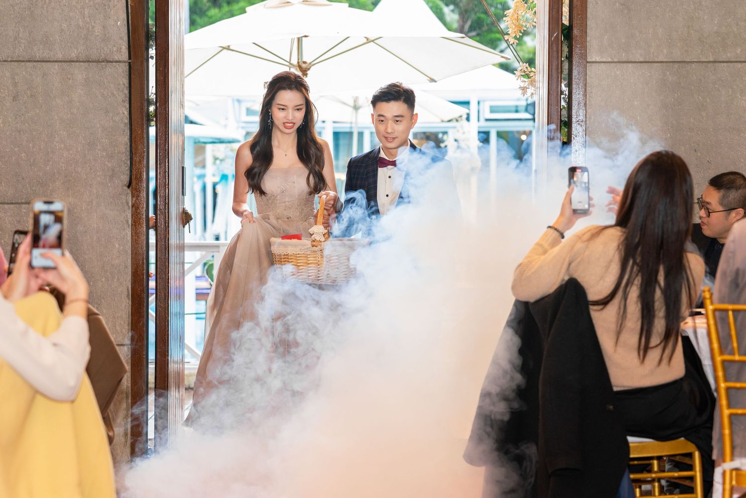People gather at an event with dramatic fog effects while photographers capture the moment at an indoor venue.
