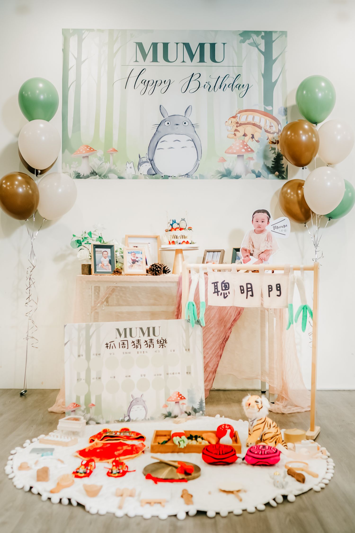 A Totoro themed birthday party setup with balloons, decorative backdrop, and snacks arranged on a white circular mat.