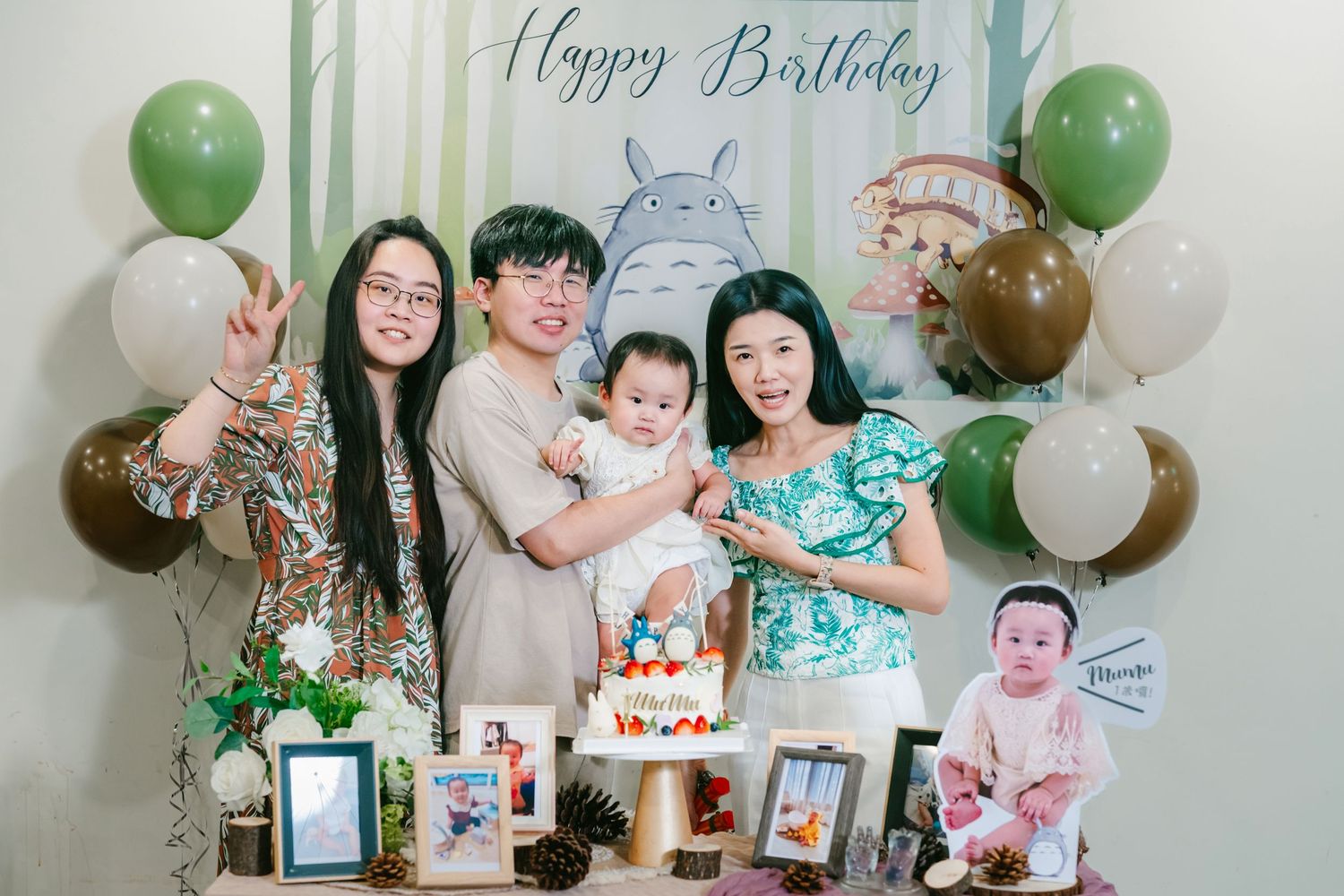Happy Birthday party decoration with green and white balloons and framed photos displayed at a first birthday celebration.