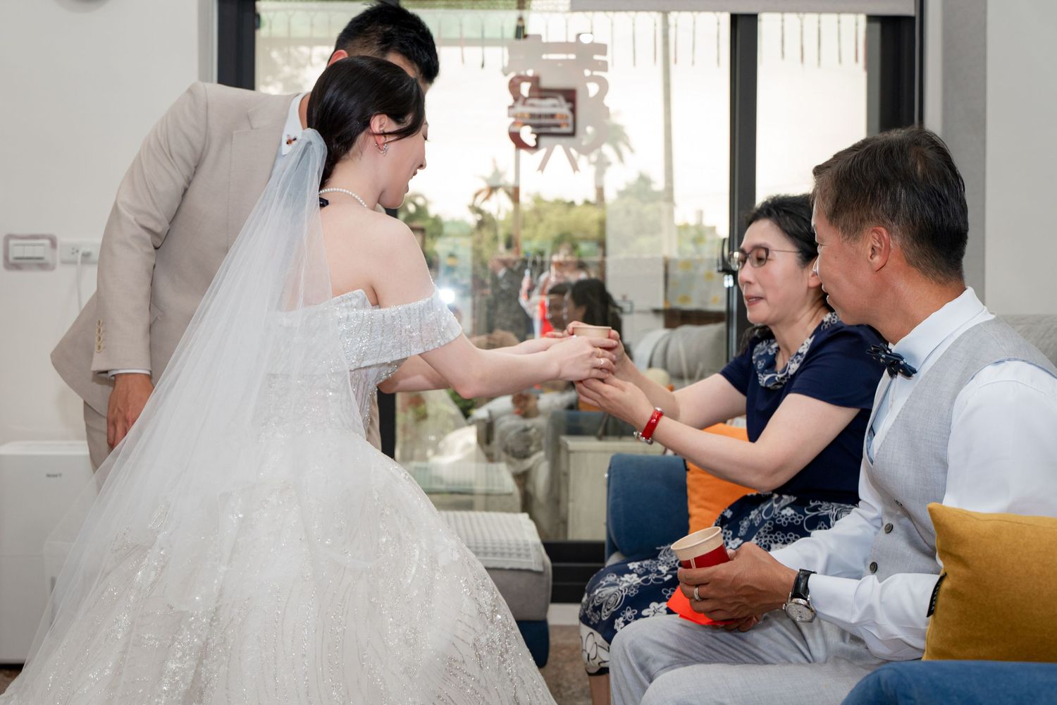 Bride in white gown holds hands with seated guests during a traditional wedding ceremony indoors.