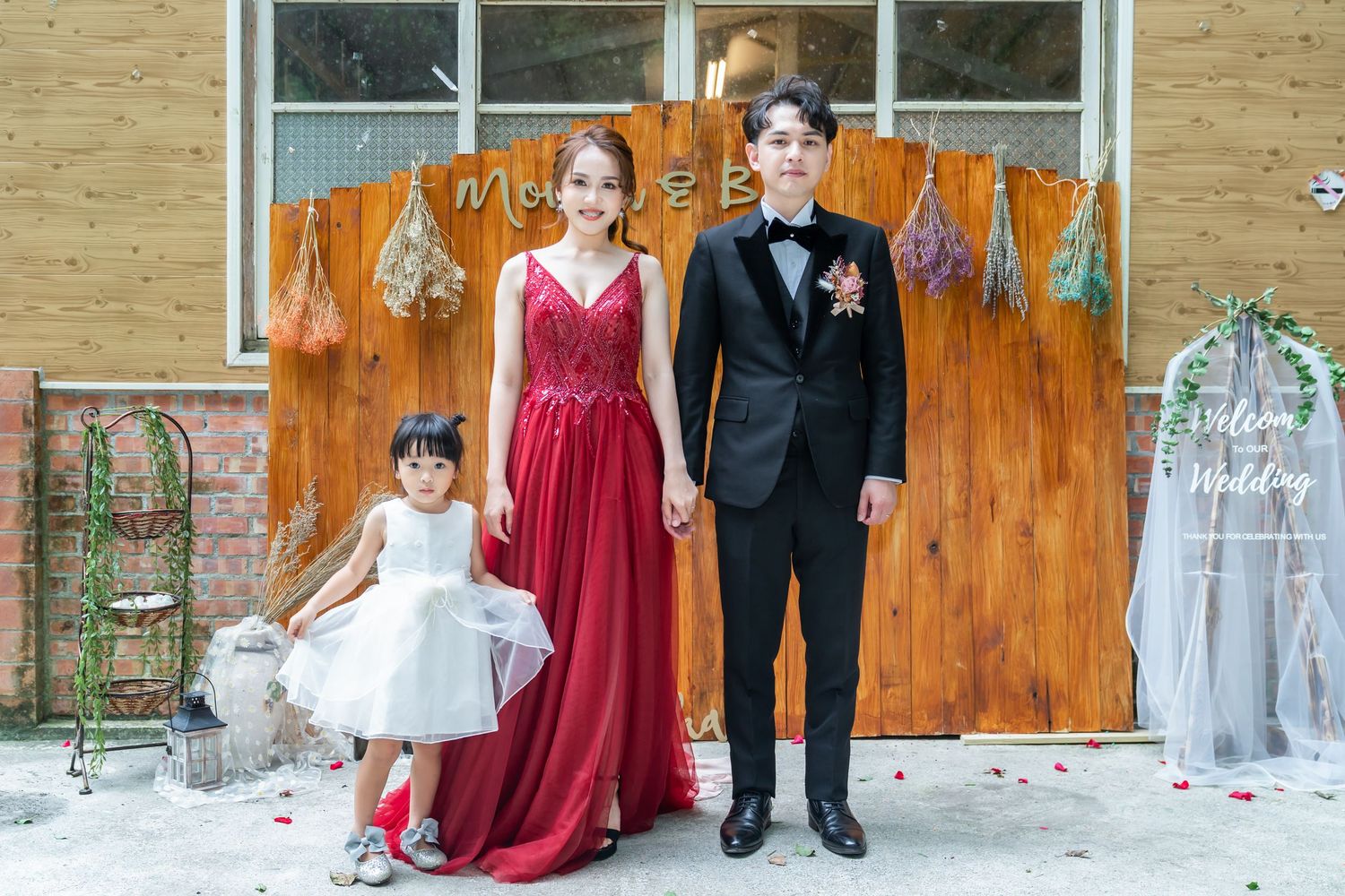 Wedding photo against rustic wooden backdrop with string lights and decorations.