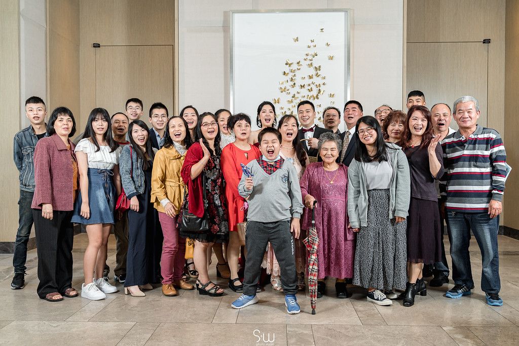 Large group photo of wedding guests posing together in front of a golden butterfly wall decoration.