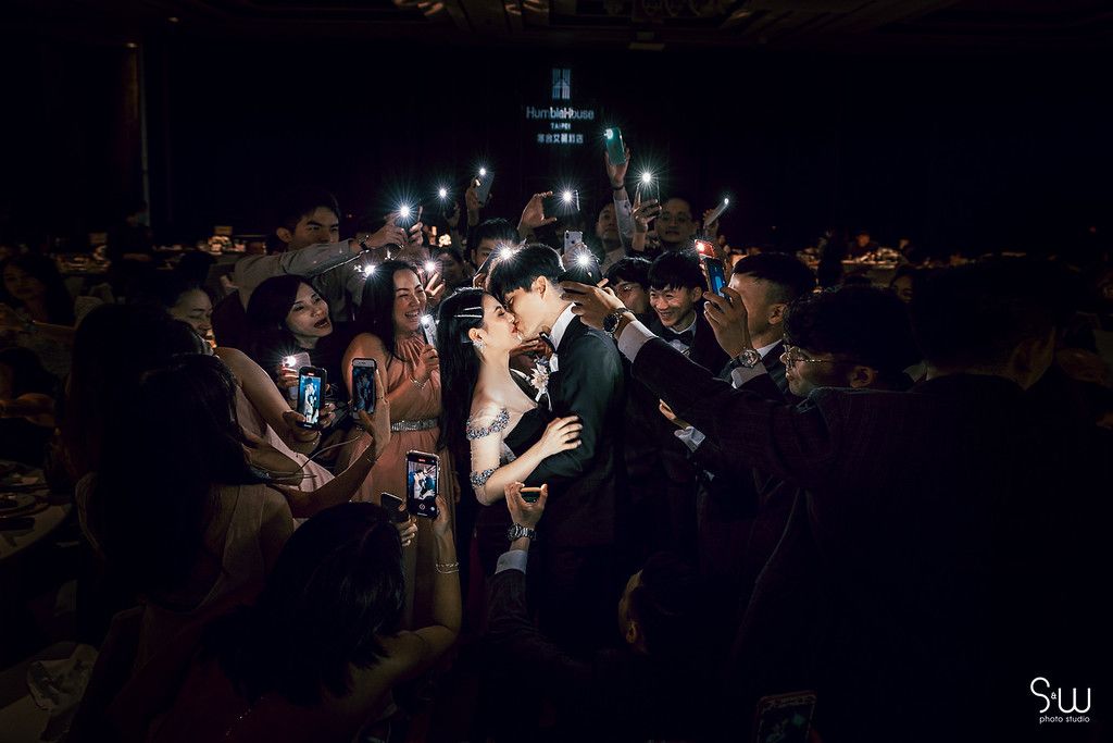 Crowd at wedding reception holds up phone lights creating a dramatic nighttime atmosphere.