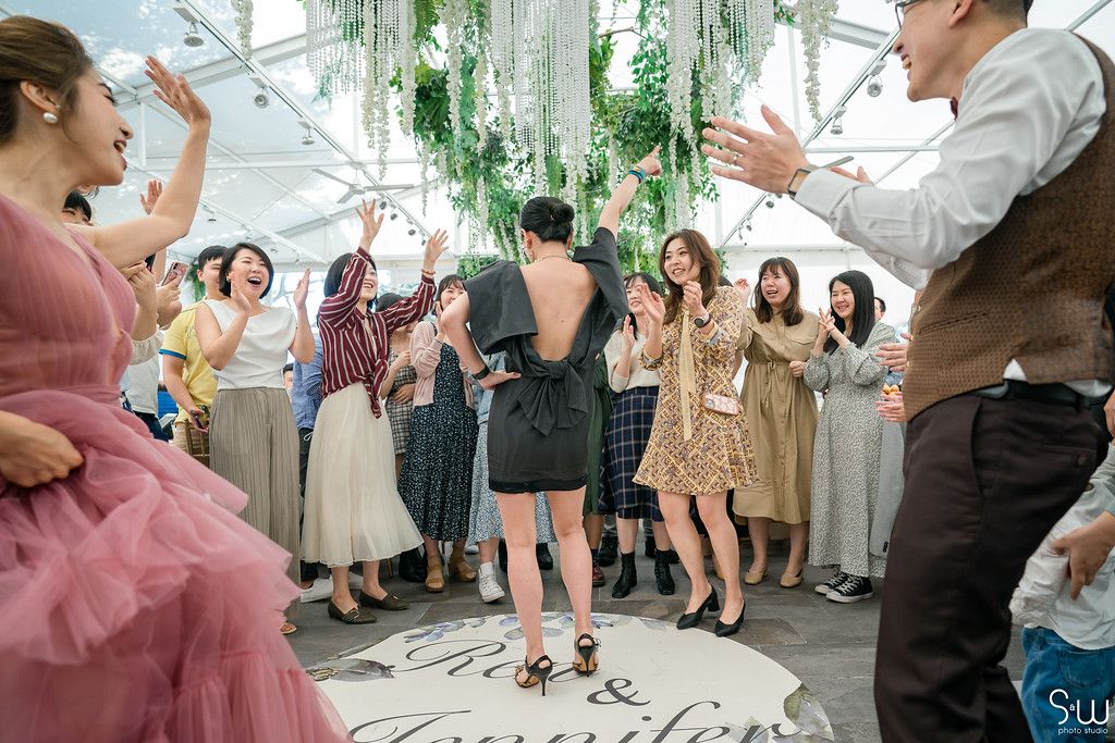 A lively reception party with guests dancing and celebrating under hanging botanical decorations.