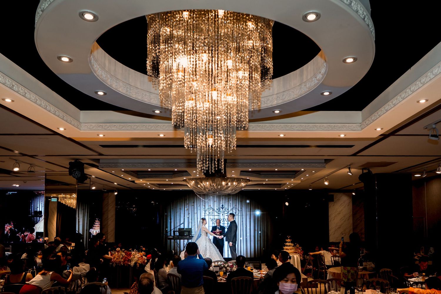 Crystal chandeliers illuminate an elegant ballroom with dark decor and circular ceiling details.