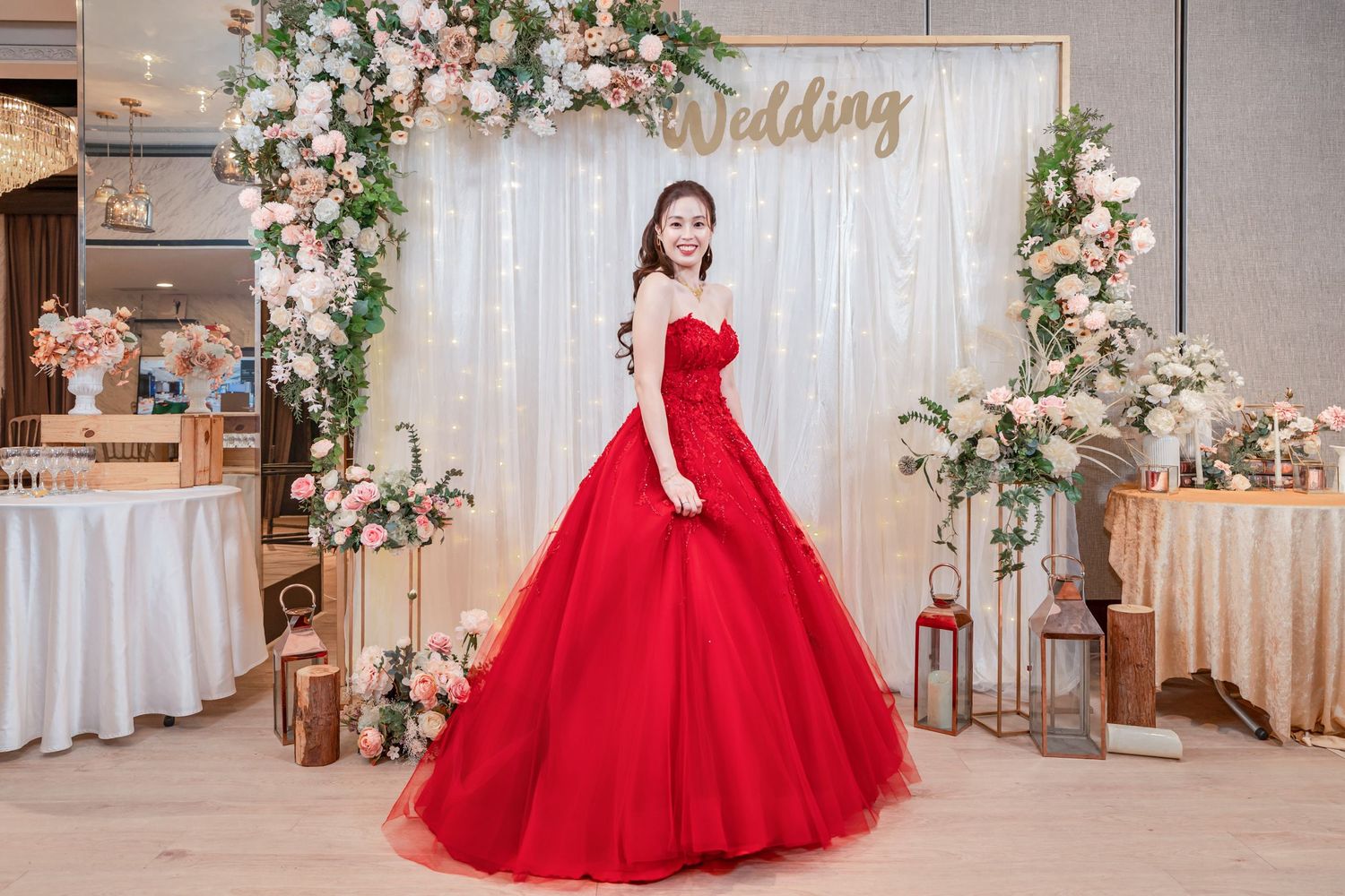 A stunning red ball gown is showcased in an elegant wedding venue decorated with floral arches and white drapes.