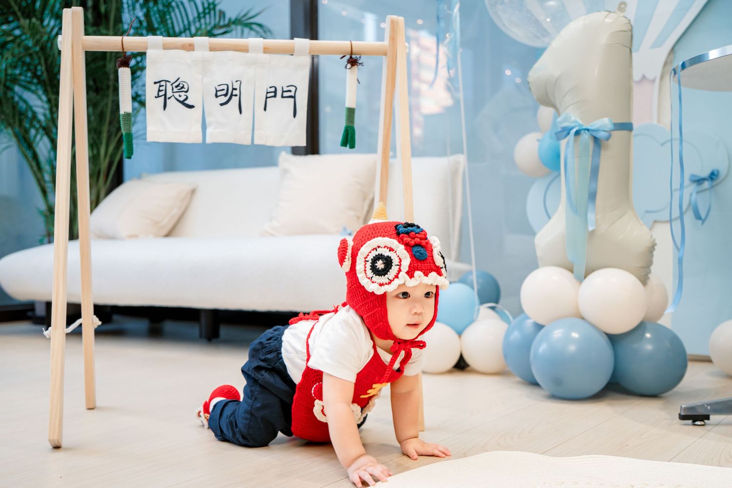 Baby in blue and white nursery crawls on floor among balloons and modern furniture.