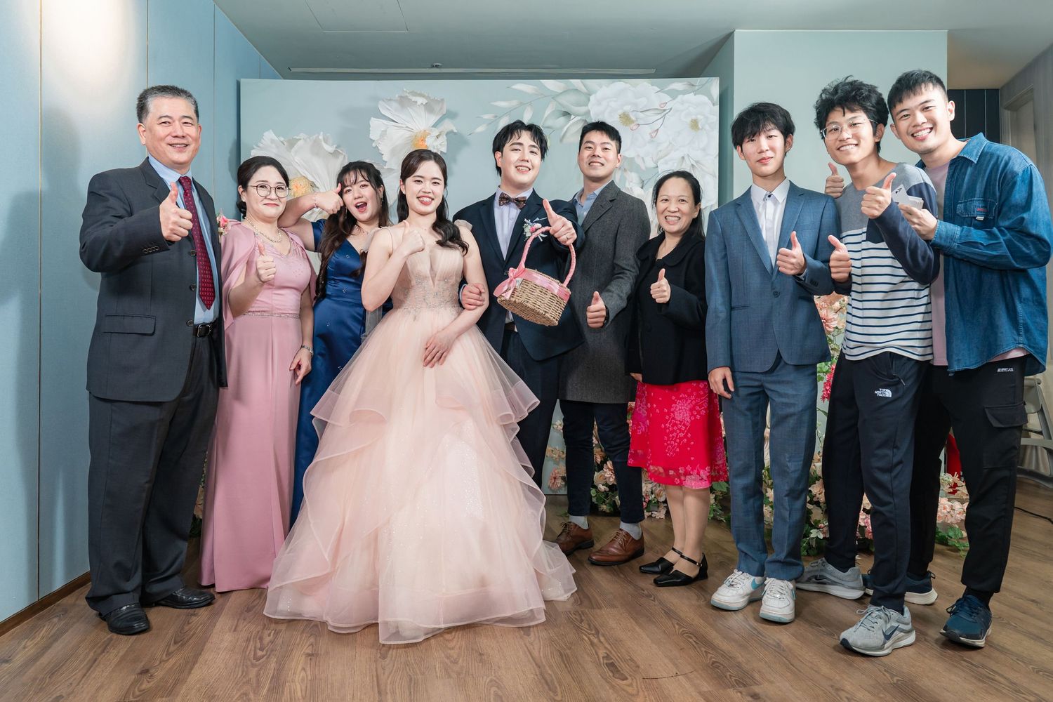 Wedding guests and attendees gather together in formal attire for a celebratory group photo at an indoor venue.