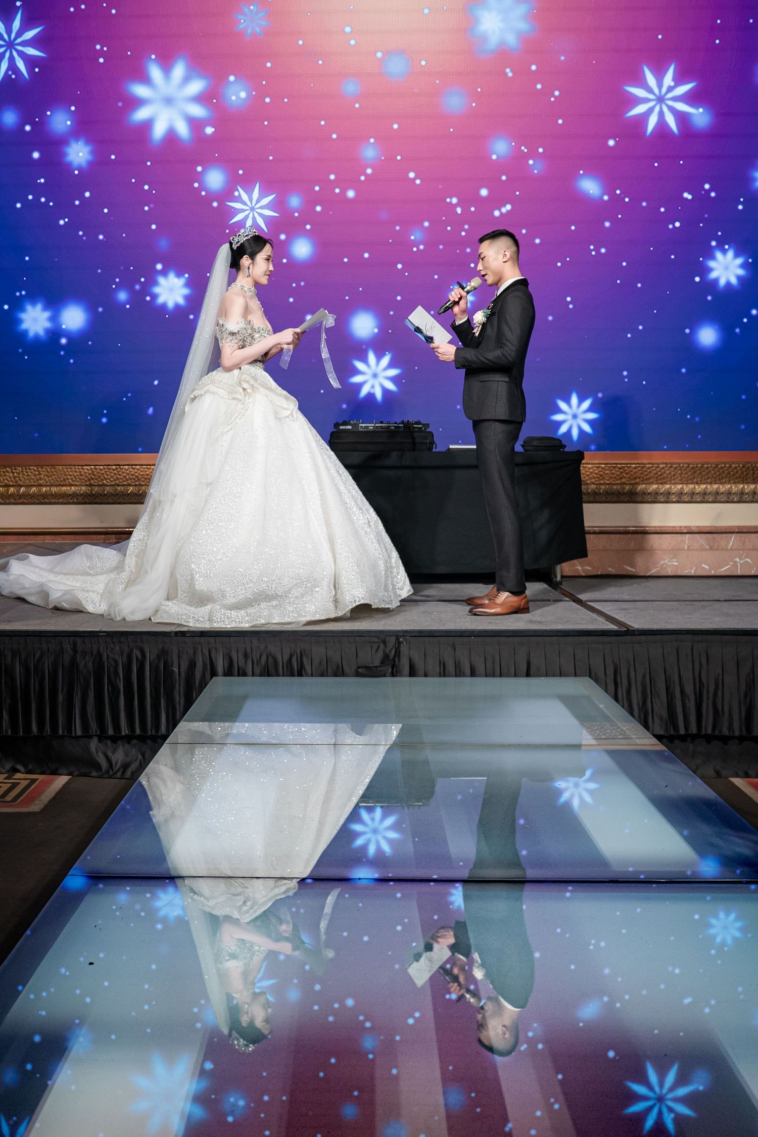 Wedding couple sits on stage with blue snowflake projections creating a magical winter wonderland atmosphere.
