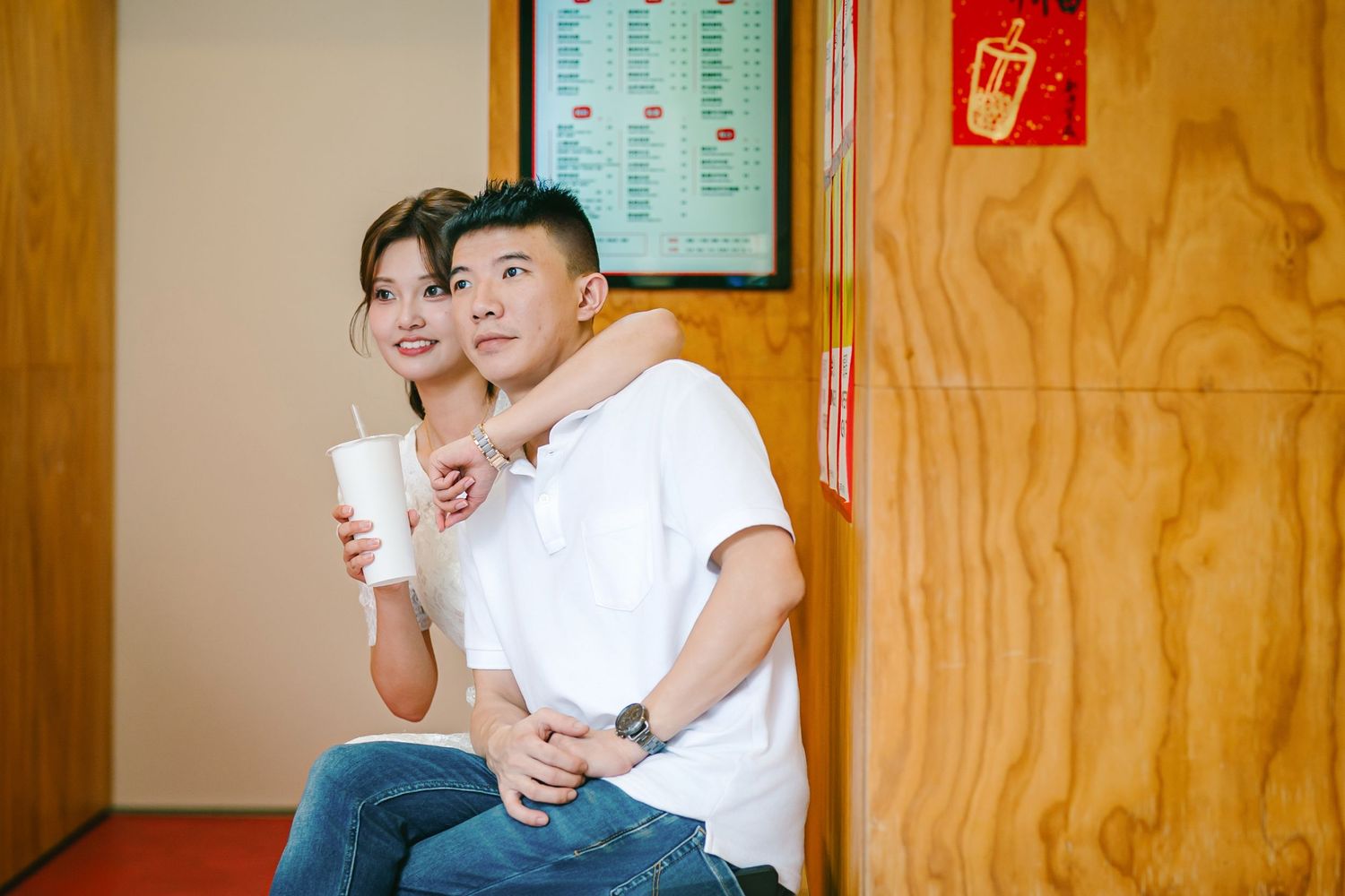 Students sit together in a classroom with wooden paneled walls and a schedule board visible in the background.