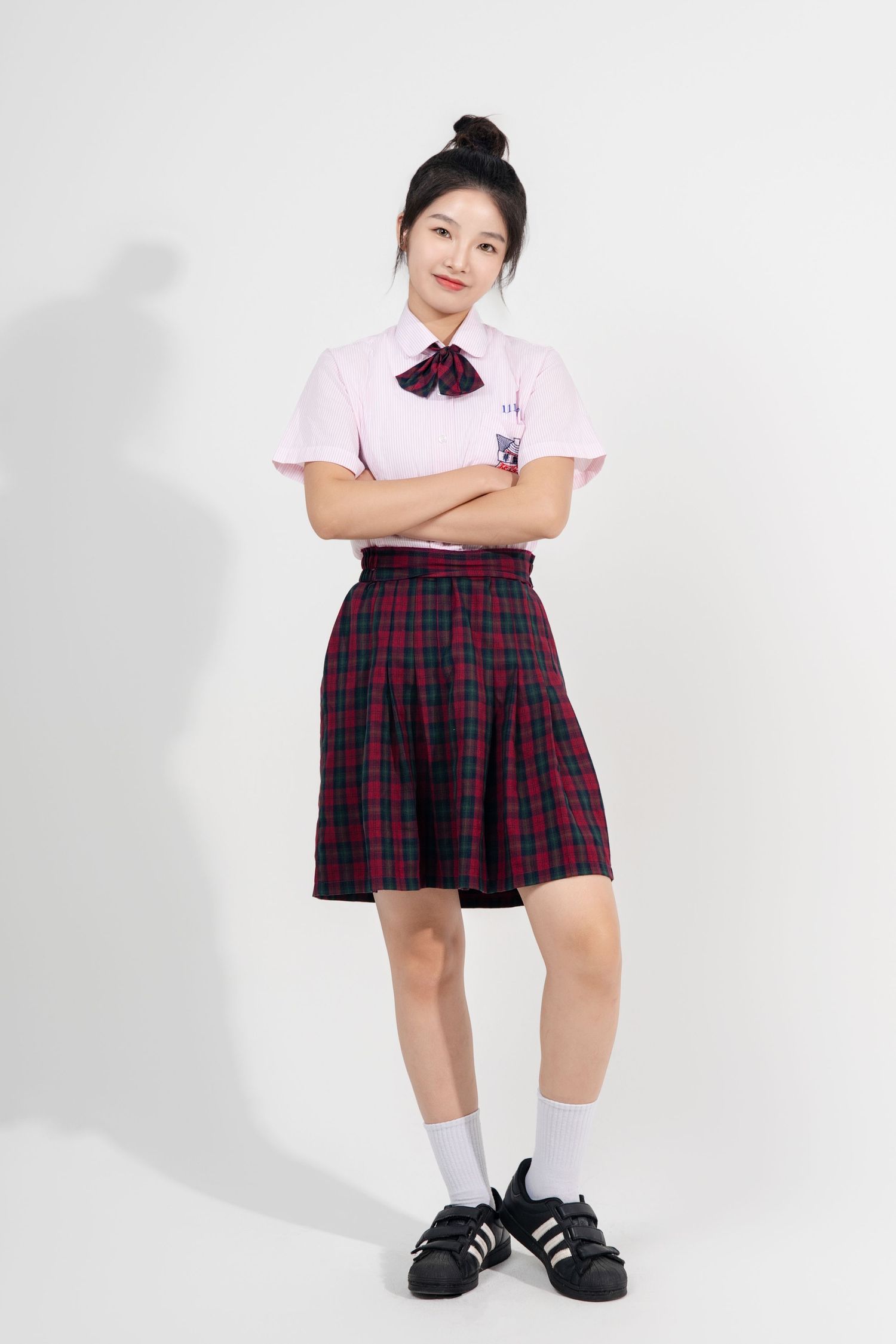 Student wearing plaid skirt uniform and pink shirt poses against white background in three different positions.
