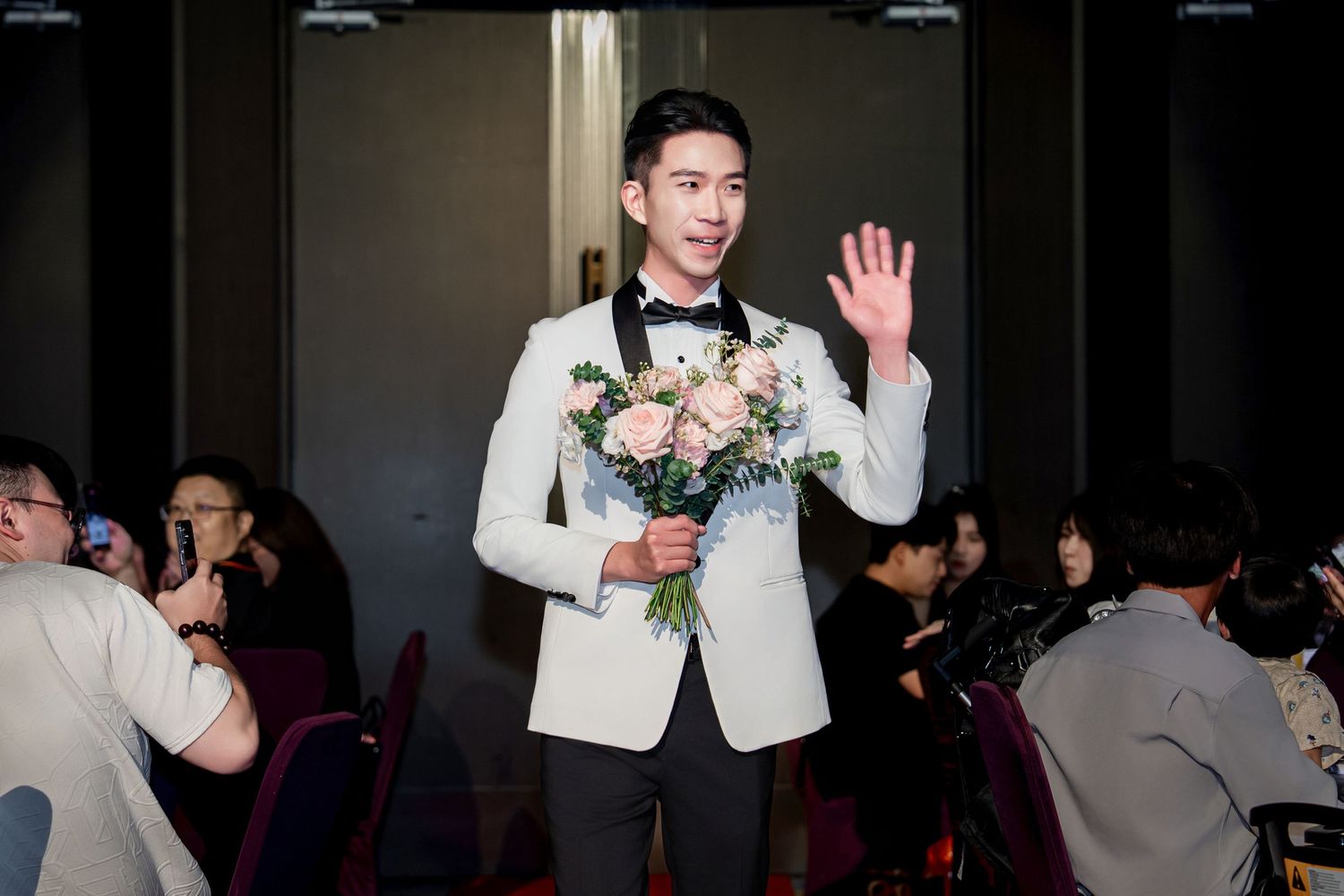 A group of people dancing and celebrating at a formal event with floral decorations and white attire.