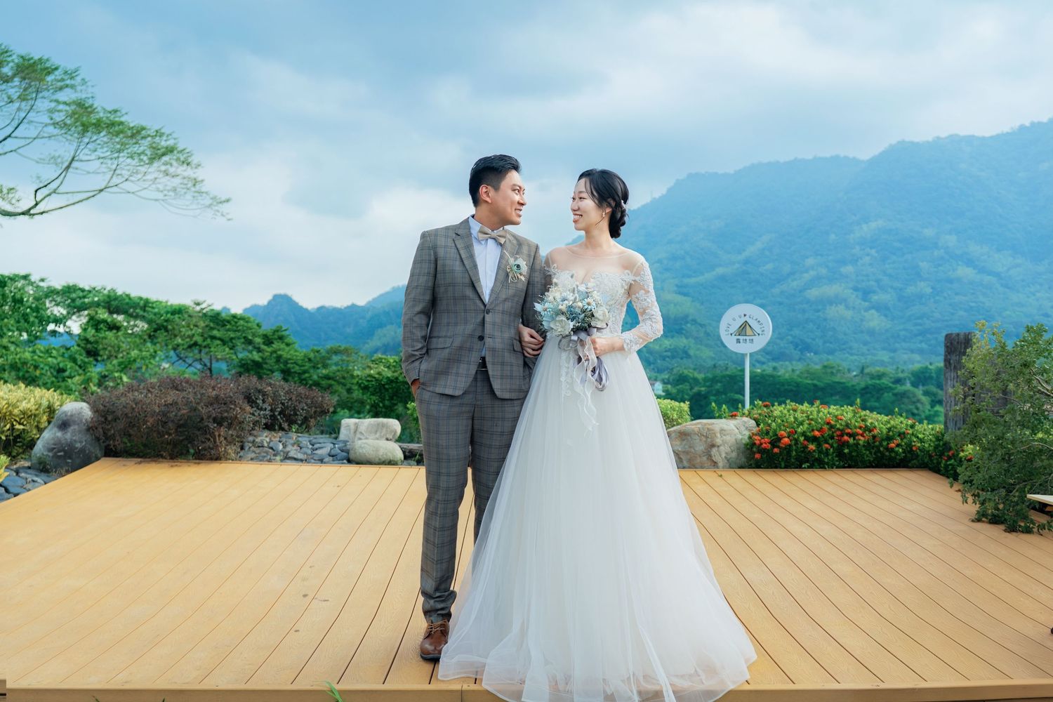 A couple shares a romantic moment on a scenic wooden deck overlooking green mountains and valleys on their wedding day.