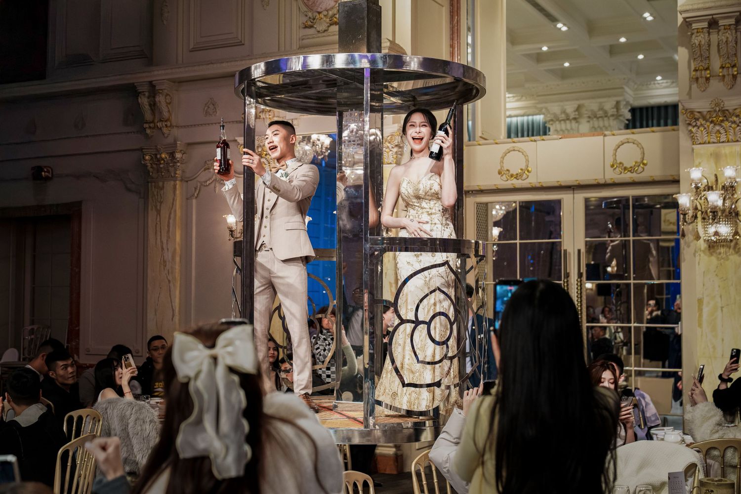 People gather at an elegant indoor venue with white decor and ornate details for a special event celebration.