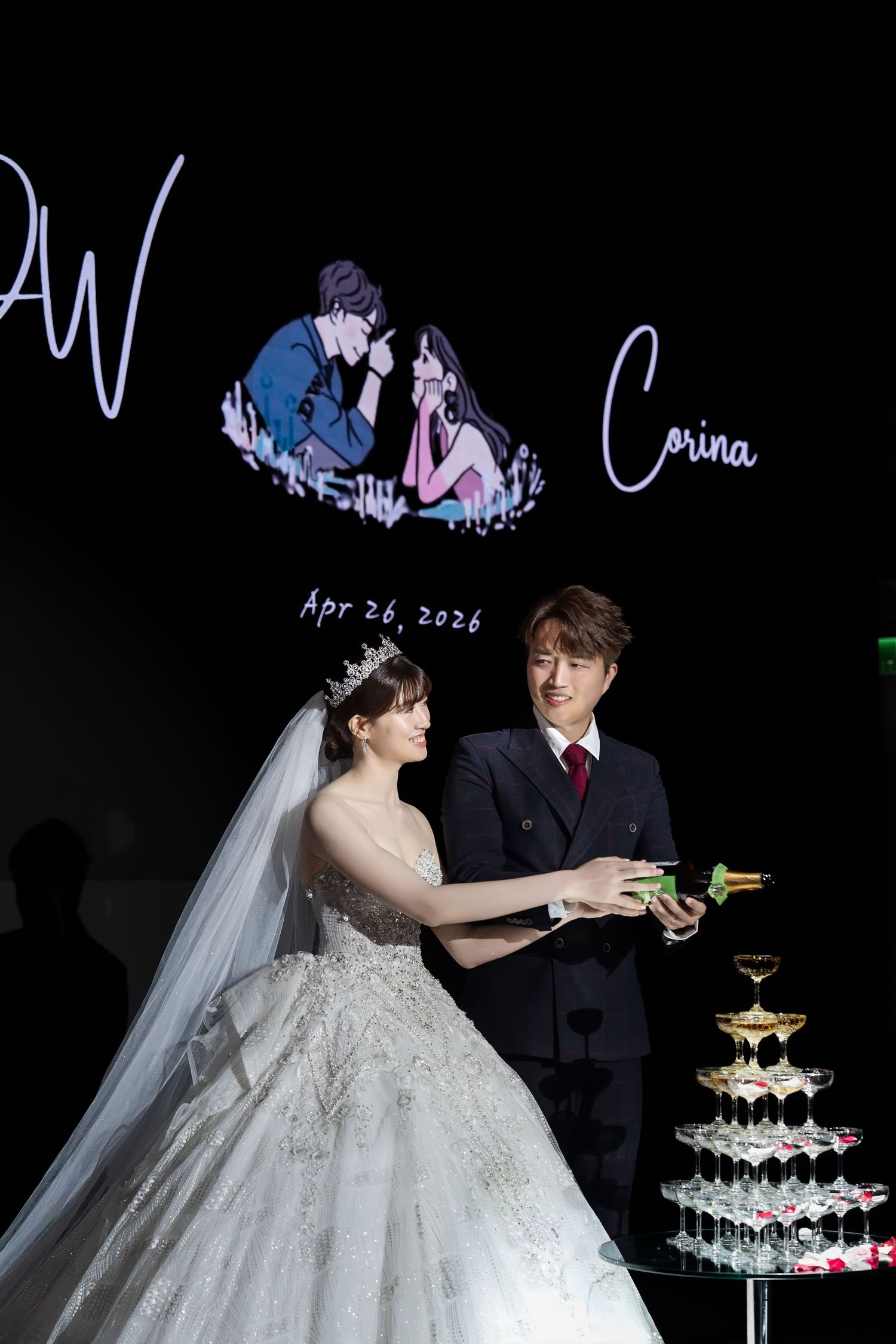 Bride and groom cutting wedding cake at elegant reception, Apr 26, 2026, with champagne tower and romantic backdrop.