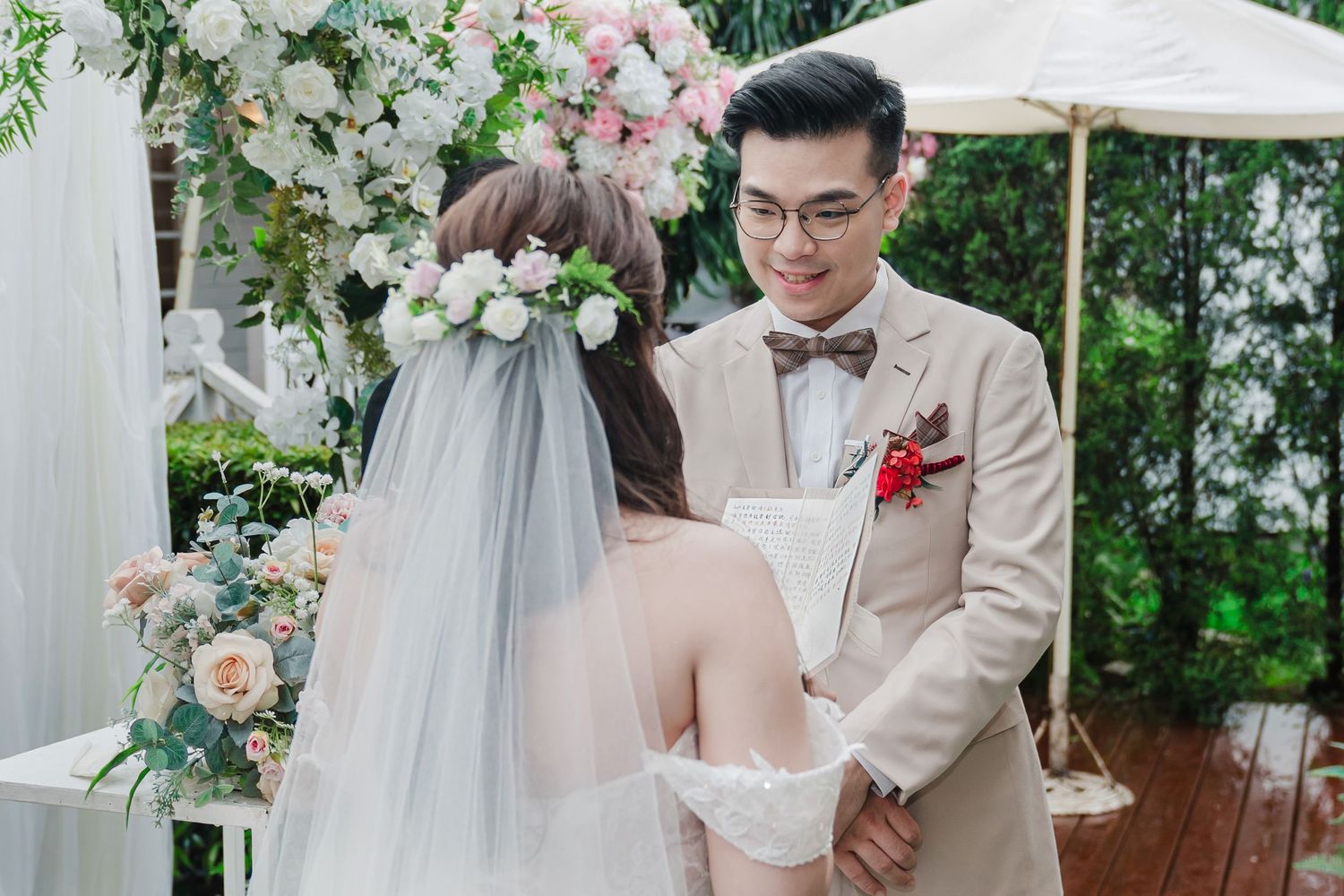Elegant outdoor garden wedding ceremony with floral arch arrangements featuring pink and white roses and flowing drapery.