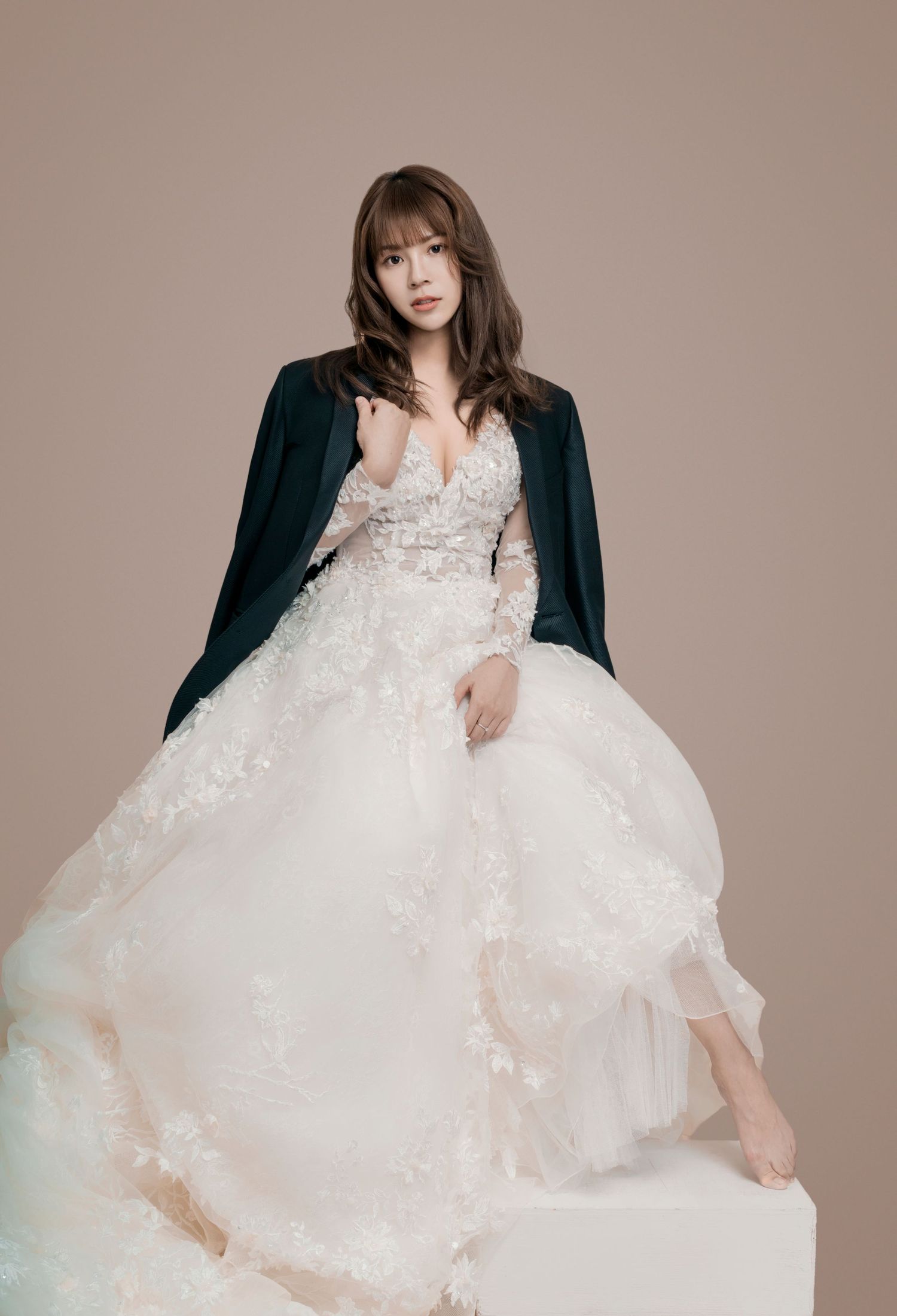 A romantic studio portrait showing a luxurious lace wedding gown with a flowing tulle skirt and dark velvet shawl.