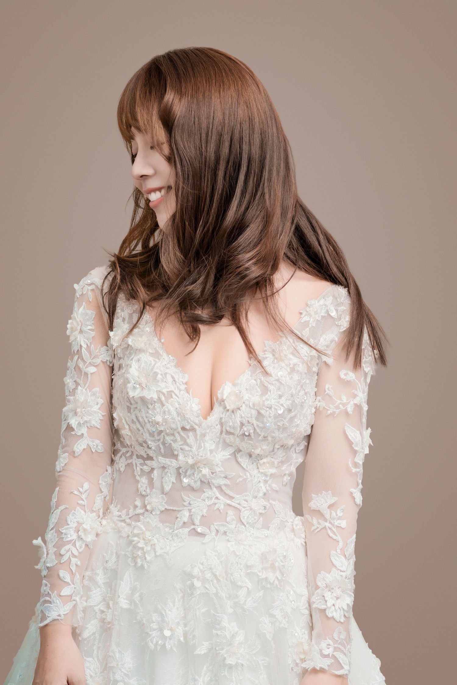 Side profile of a bride wearing a long sleeve white lace wedding gown with sheer details and floral appliques.