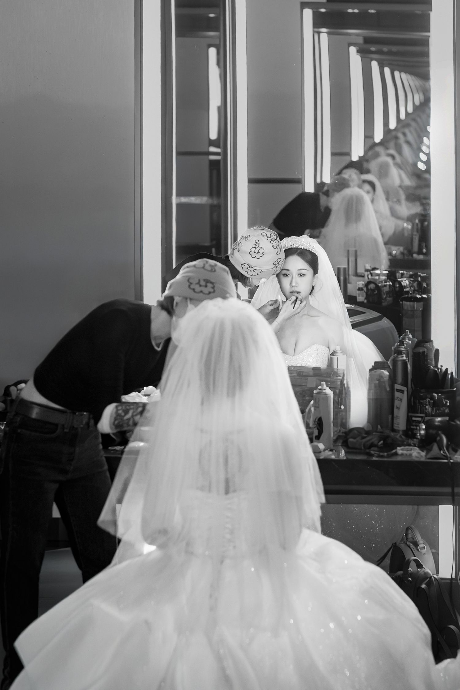 Black and white image showing a wedding dress preparation scene with flowing white veils and tulle in a dressing room.