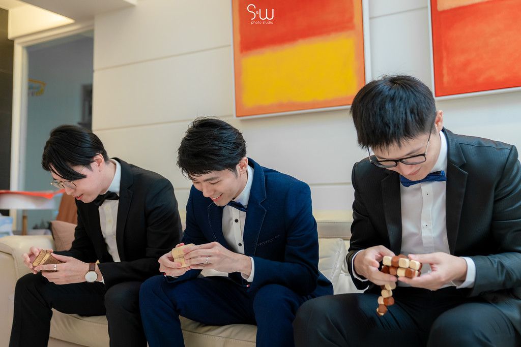 Three groomsmen in formal attire sitting together looking at their phones.