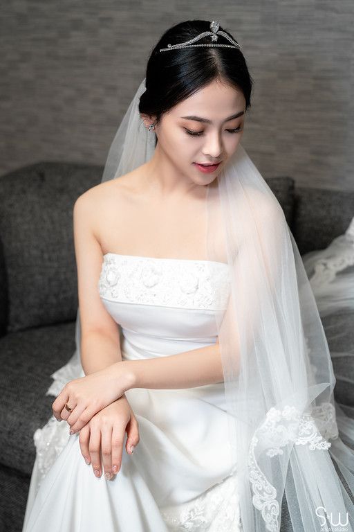 A bride in a white strapless wedding gown and veil looking down with elegant makeup.