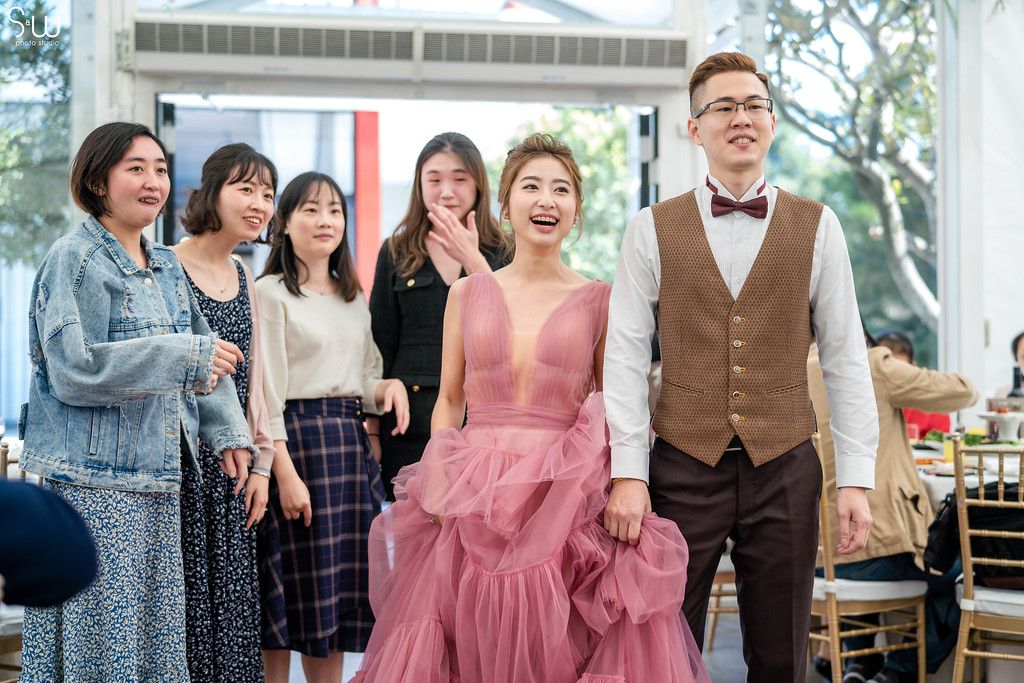 Wedding party poses together under white tent with decorative greenery.