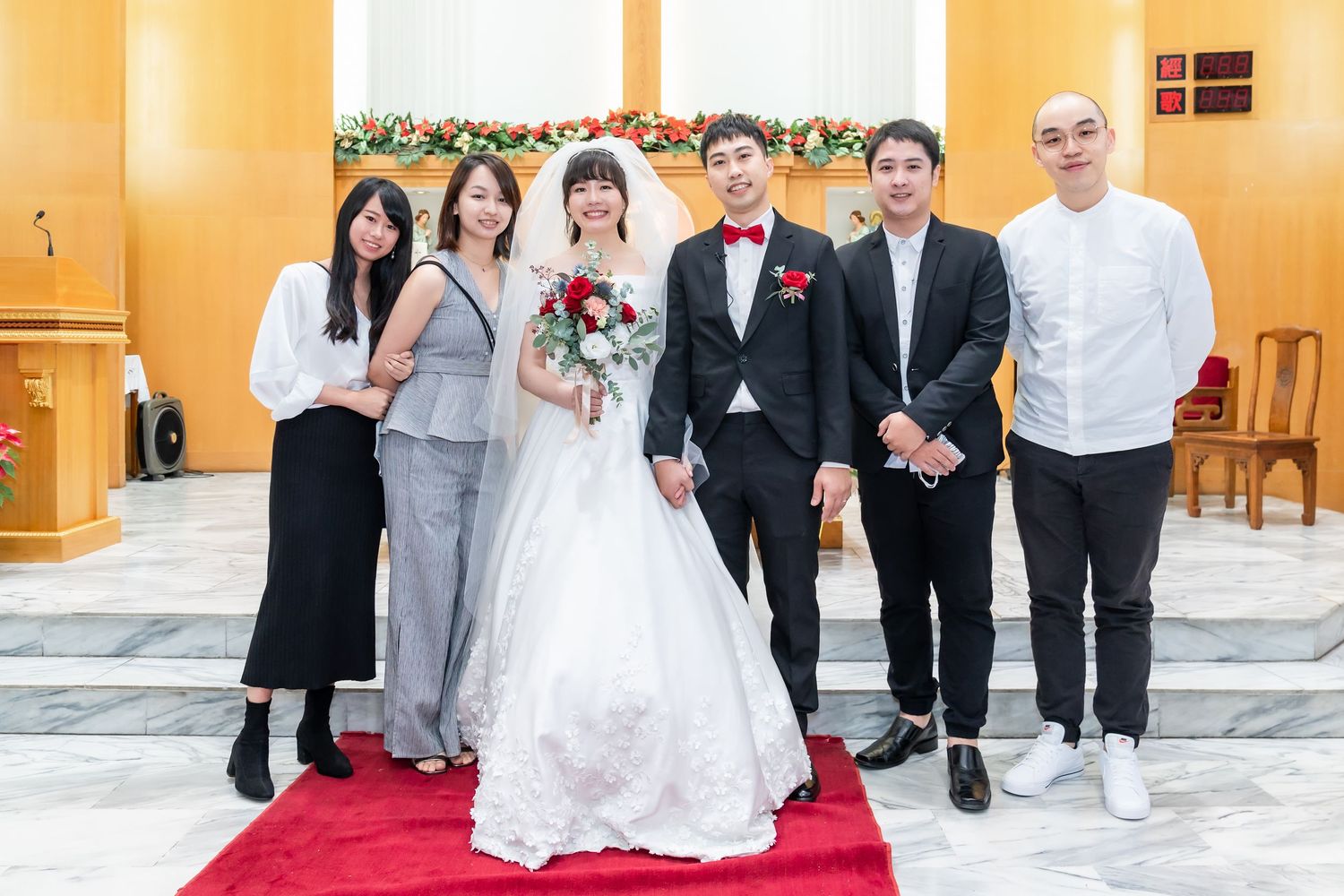 Wedding party and guests pose formally on red carpet in church with yellow walls.