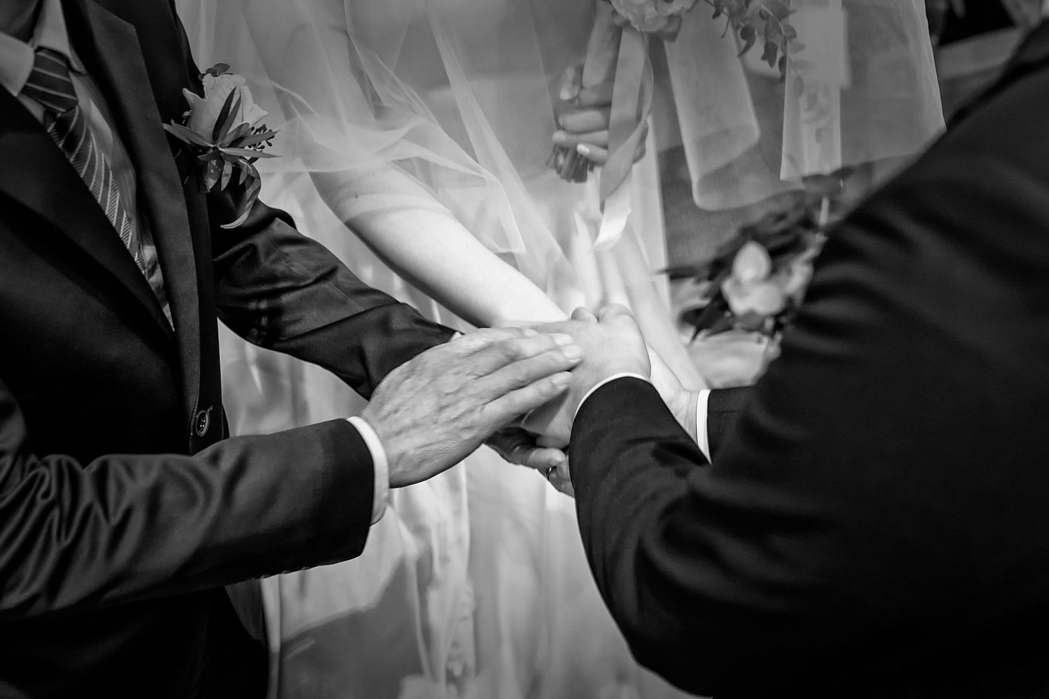 Black and white close-up of hands during wedding ceremony ritual.