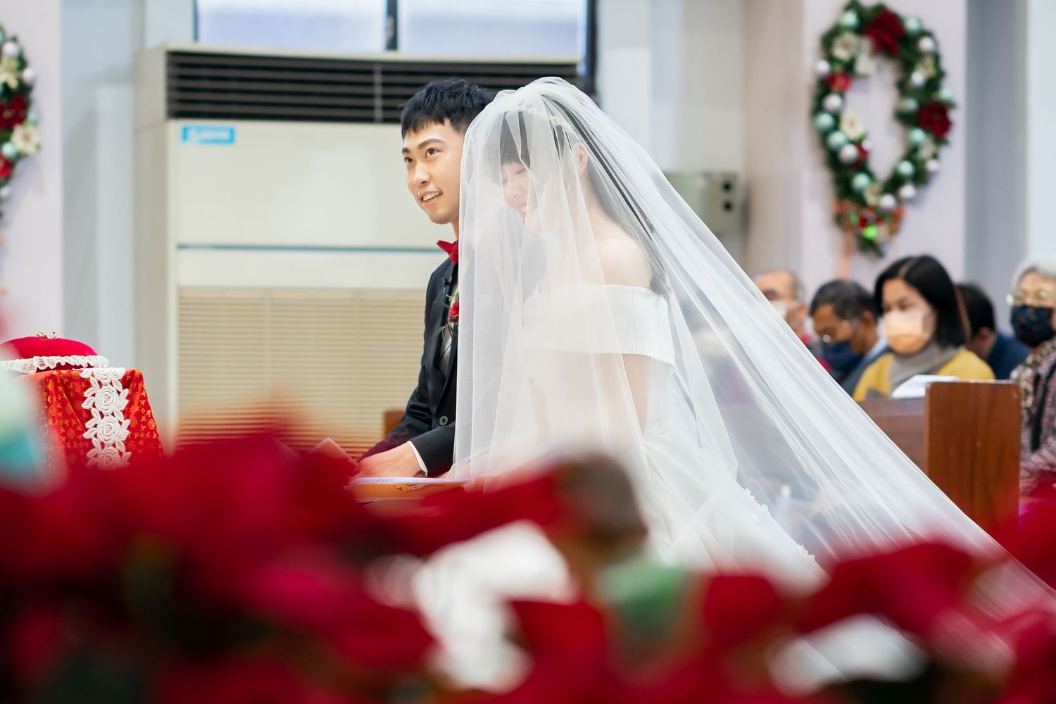 A wedding ceremony in a church adorned with festive red decorations and wreaths.