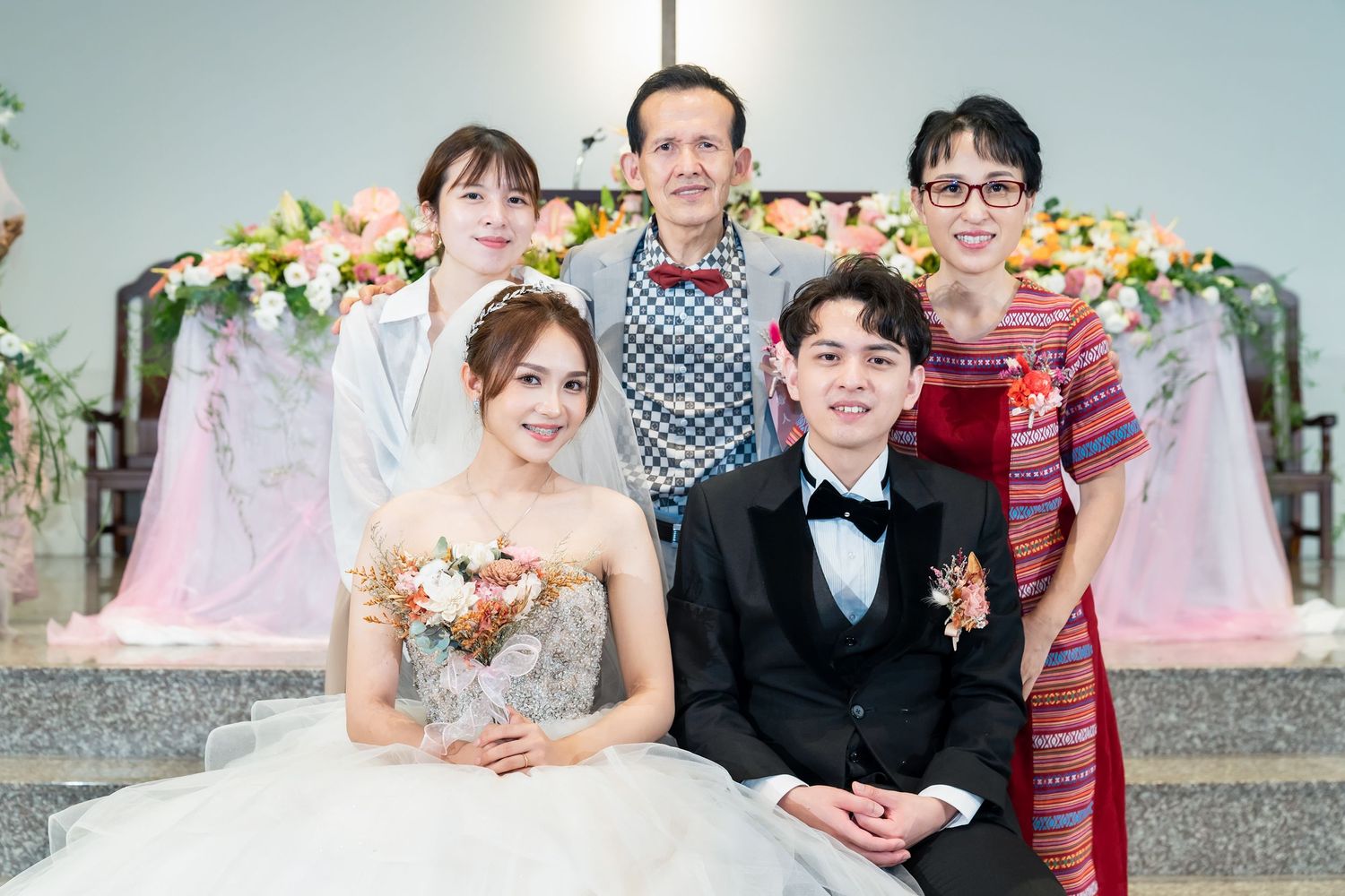 Wedding group photo with international guests against pink and white floral decorations.