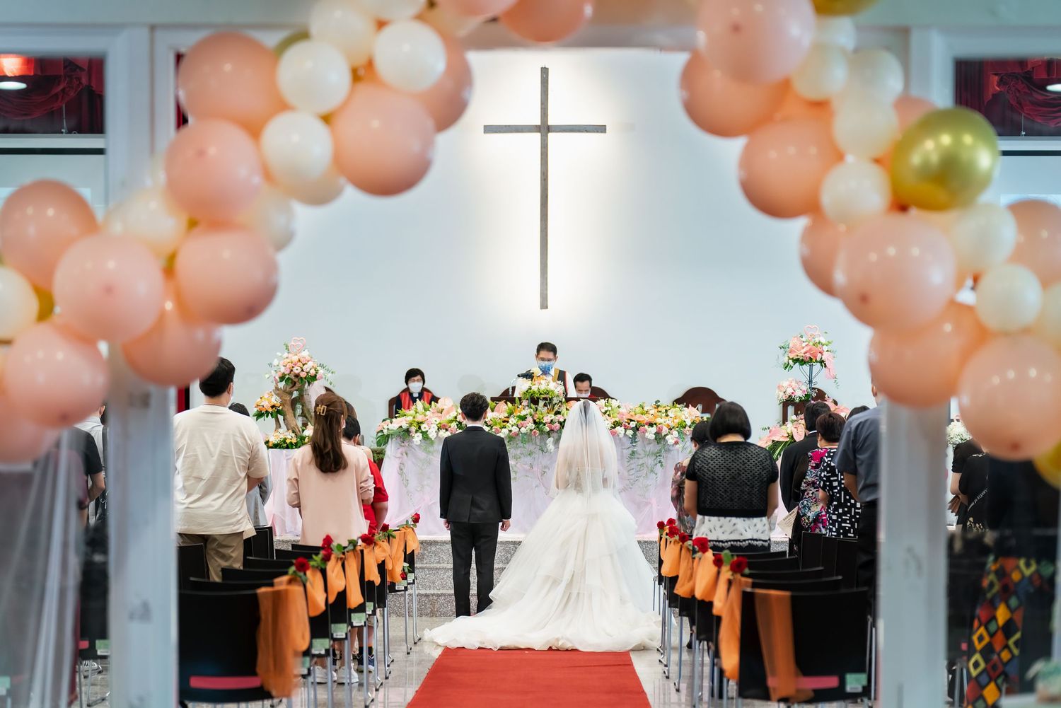 Wedding ceremony in a church with peach balloon arch and cross centerpiece.