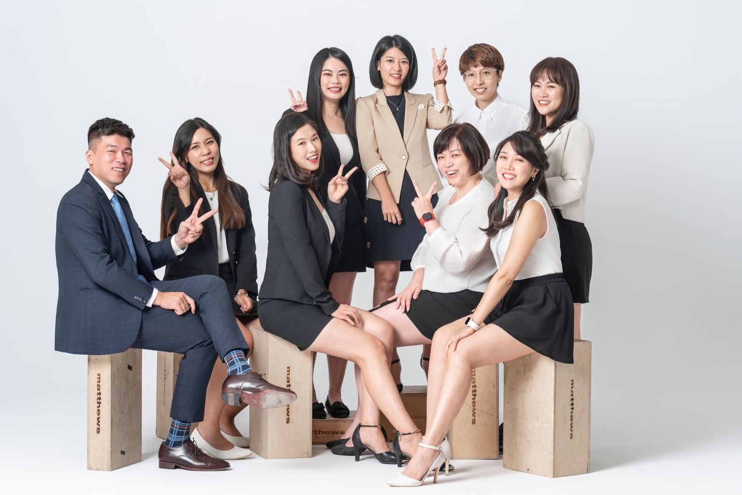 A group of business professionals in formal attire pose together on wooden blocks against a white background.