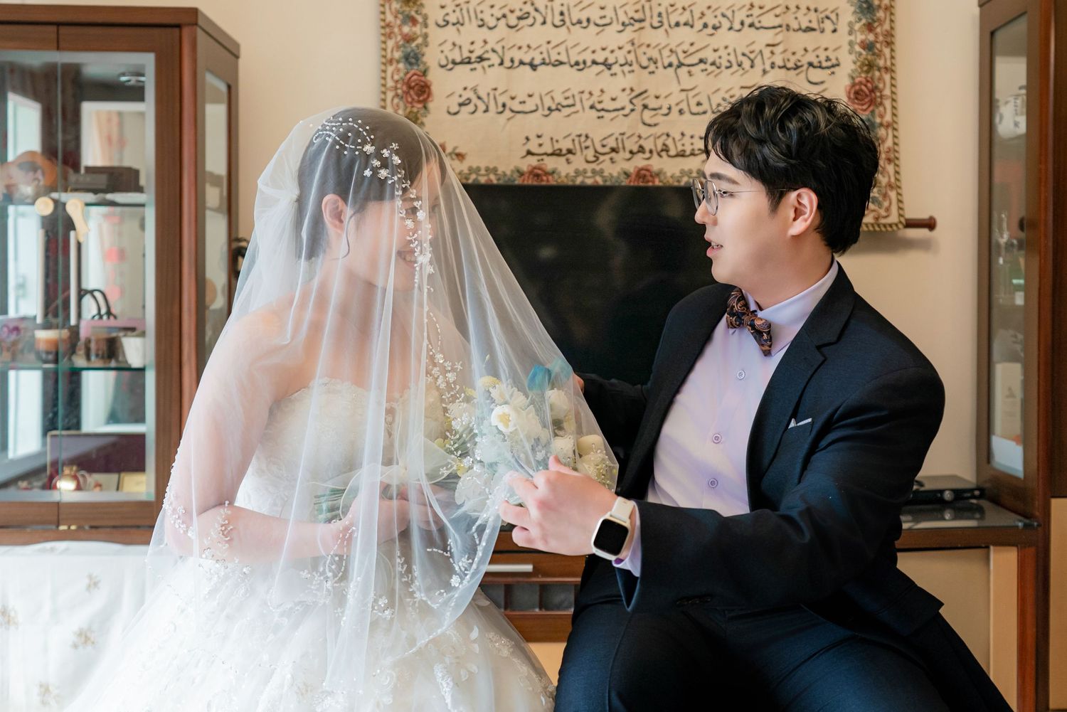 A traditional wedding ceremony takes place in an elegant venue with Arabic calligraphy on the walls.