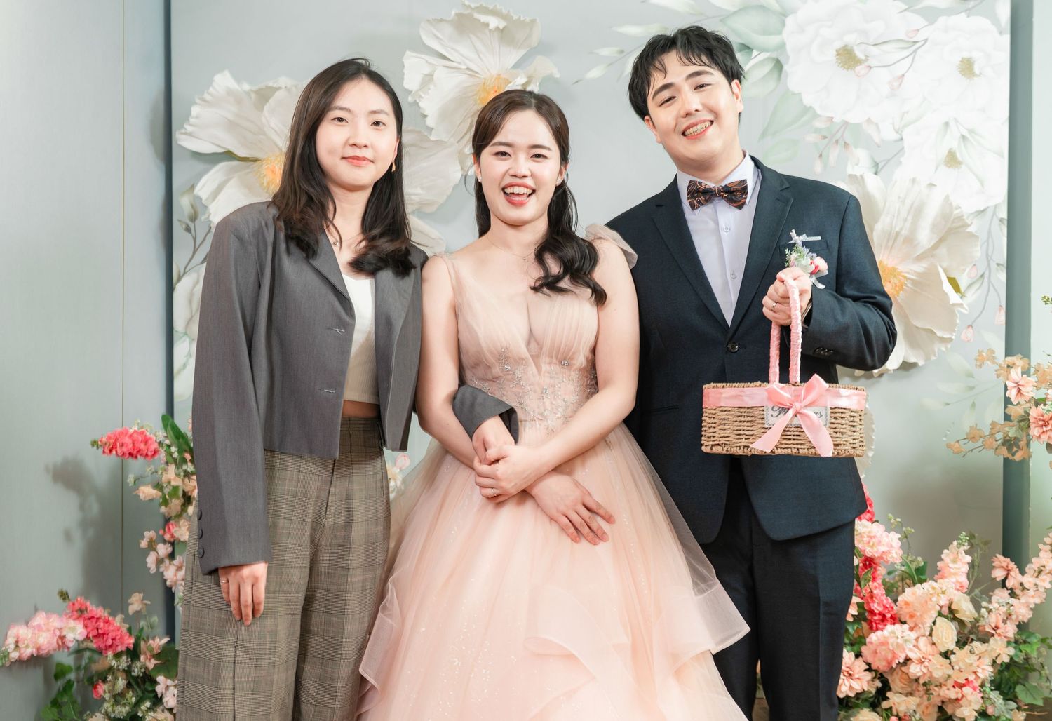 Wedding party poses in elegant formal attire against floral backdrop at an indoor venue.