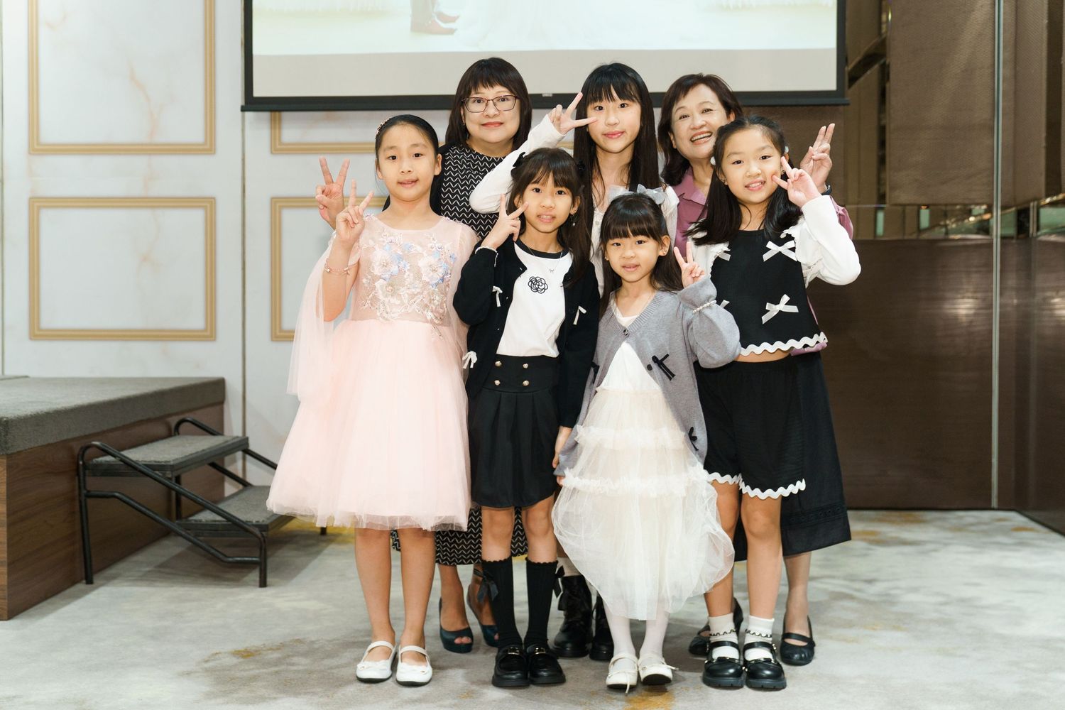 A group of children in formal attire pose together in an elegant indoor venue with marble floors and gold accents.